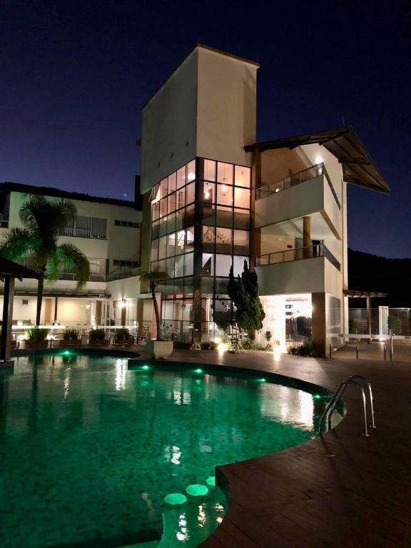 Vista noturna de um hotel com piscina iluminada. Os prédios têm paredes de vidro e varandas.
