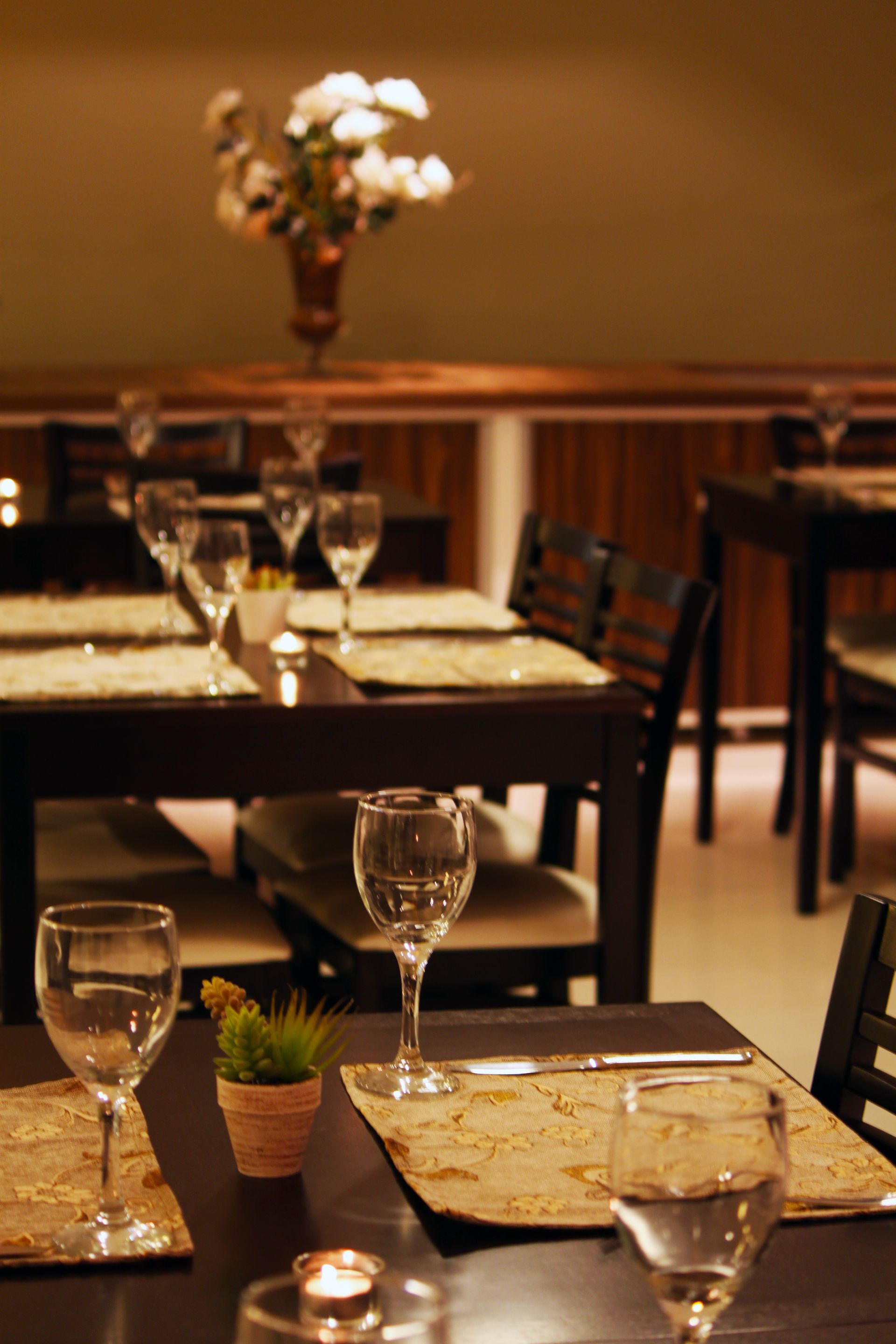 Restaurante vazio com toalhas de mesa brancas, paredes marrons e cadeiras de madeira escura.