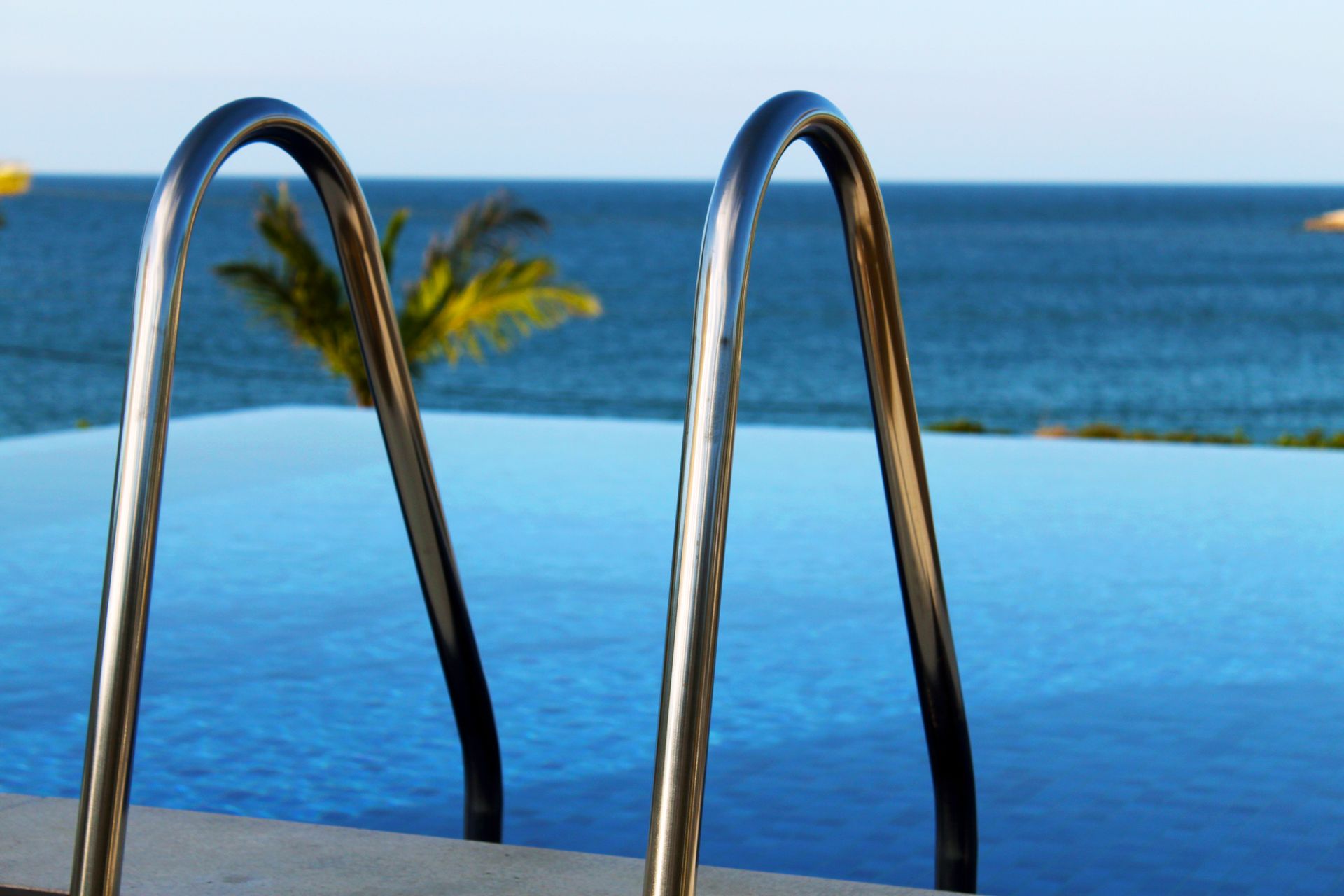 Escada de piscina sobre água azul, com vista para o oceano em um dia ensolarado.