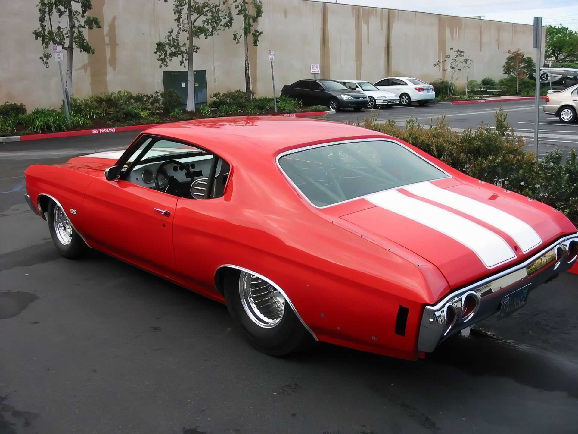 Red classic muscle car with white racing stripes parked in a lot