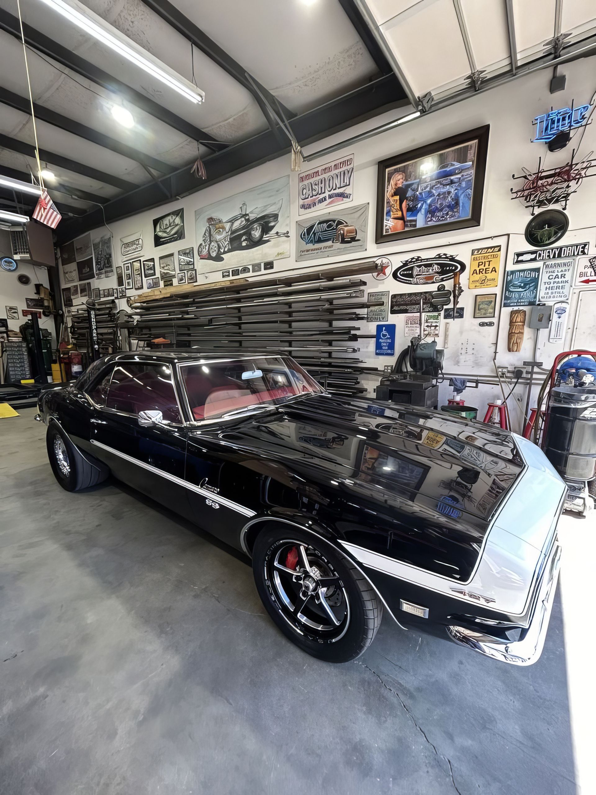 Black classic car in a garage showroom with wall-mounted memorabilia and tools