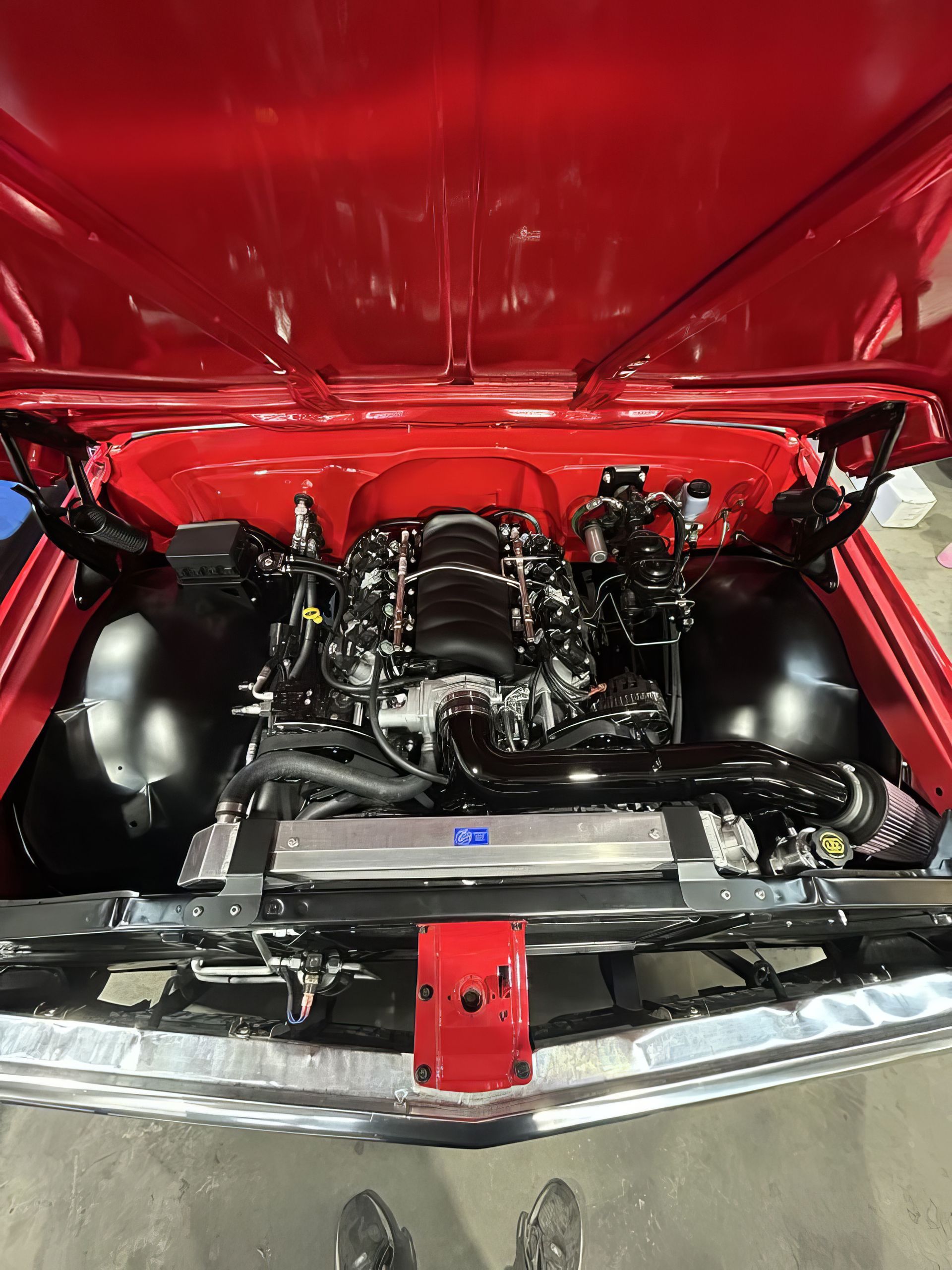 Custom car engine bay under a red hood, with a chrome radiator and black engine components.