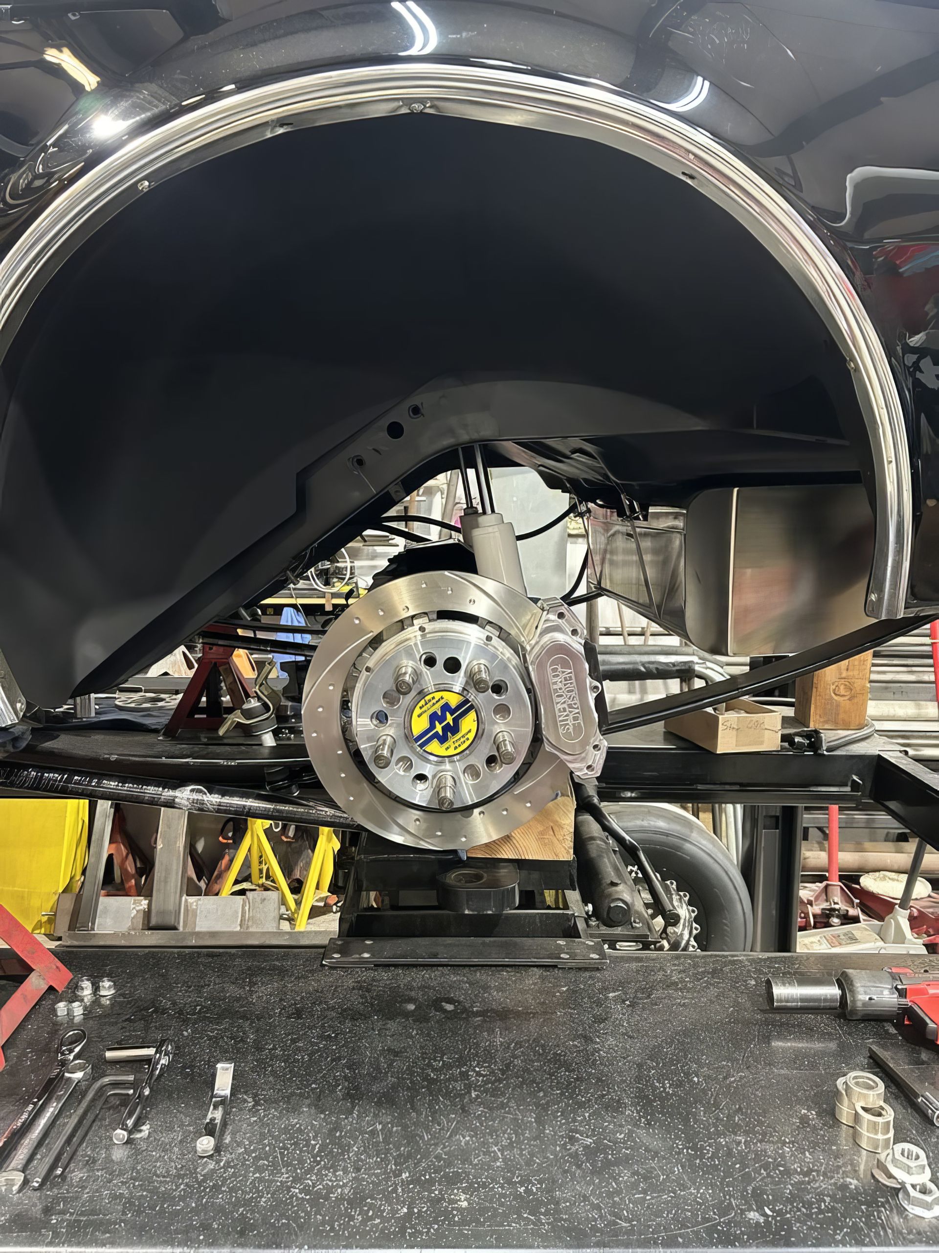 Auto wheel hub and suspension assembly inside a workshop, with a yellow jack stand visible