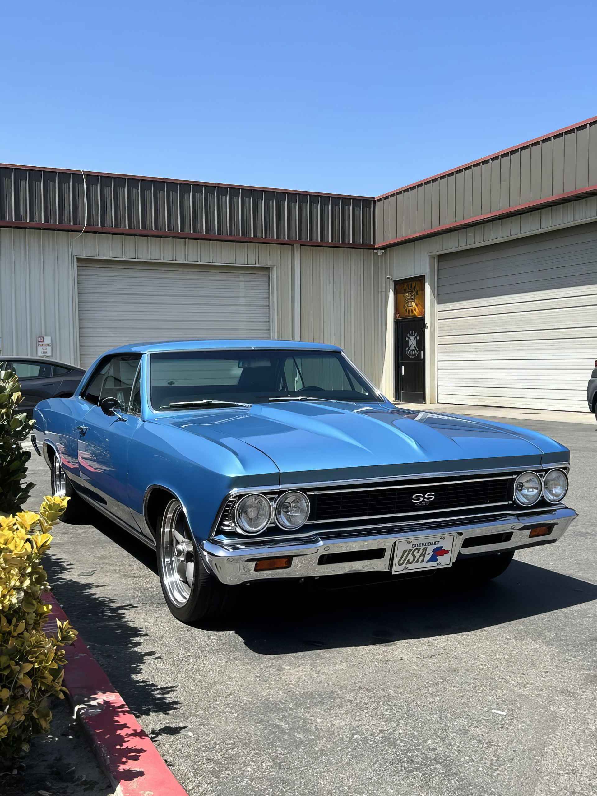 Blue classic car parked outside a garage under a clear sky
