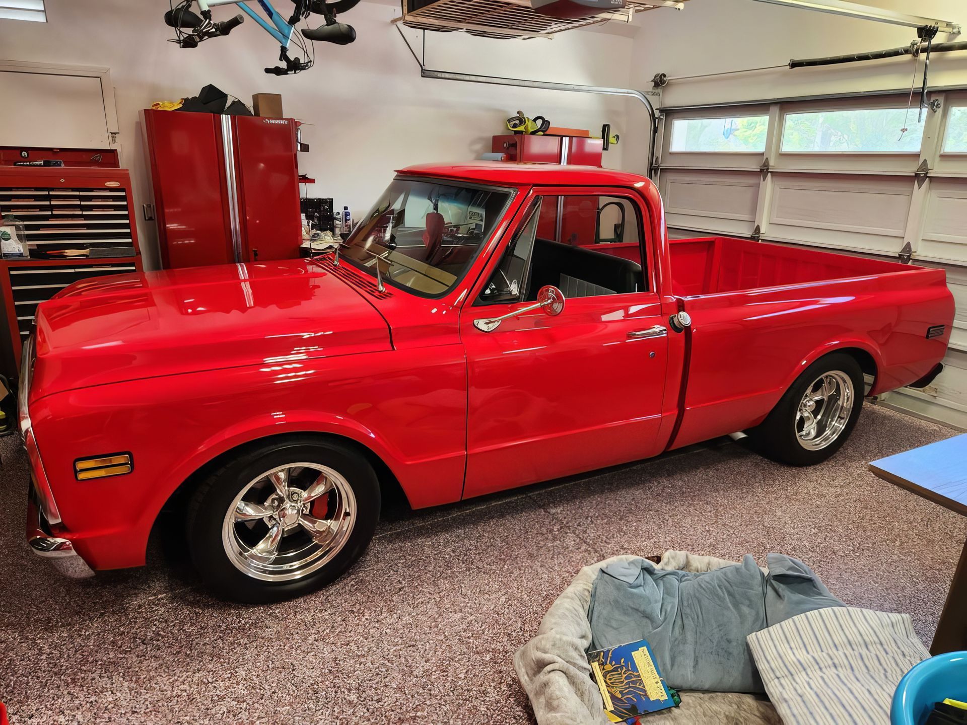Red vintage pickup truck in a garage with tools and cabinets, viewed from the side.