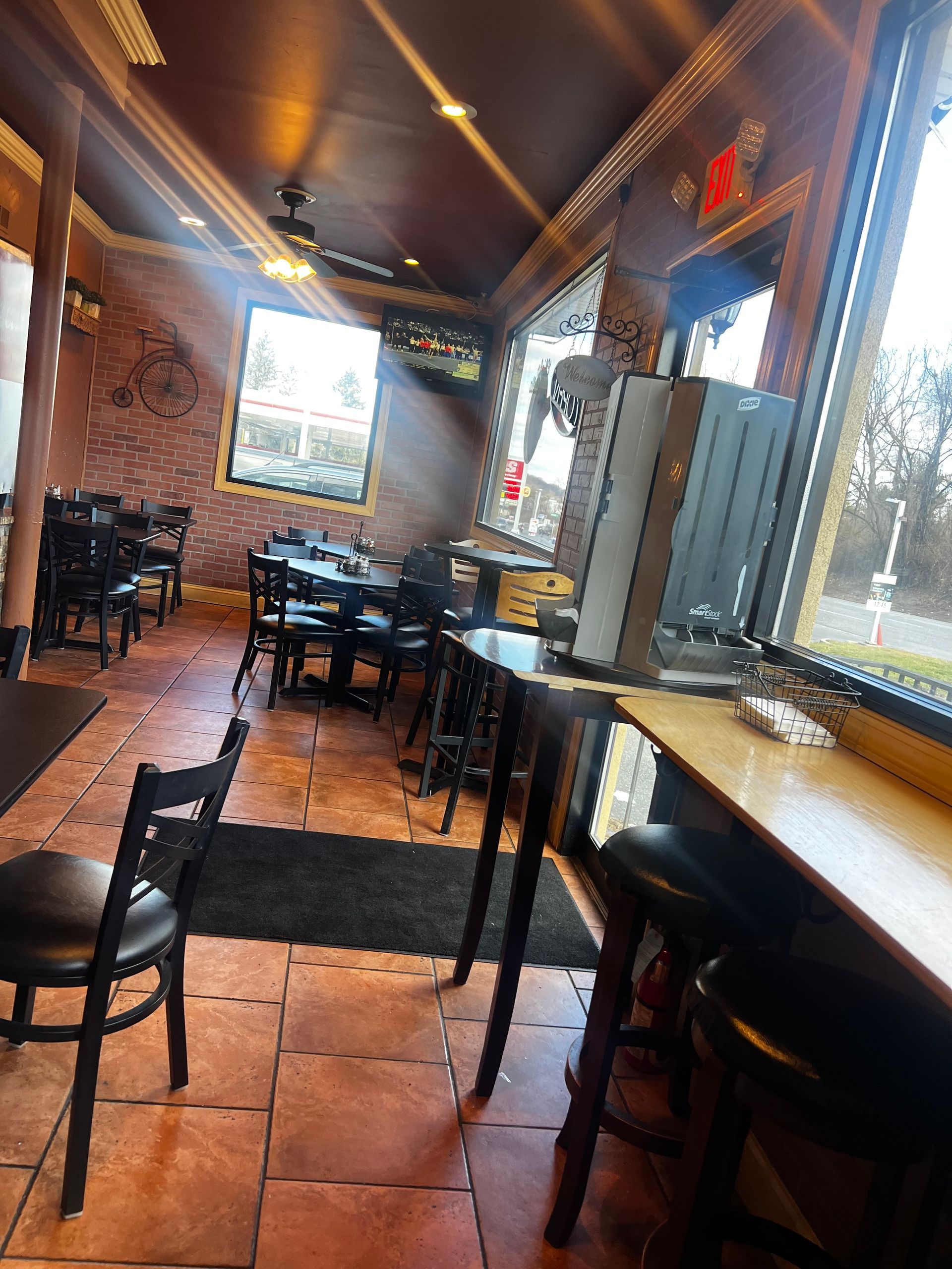 Cozy restaurant interior with wooden tables, black chairs, warm lighting, and a long window counter.