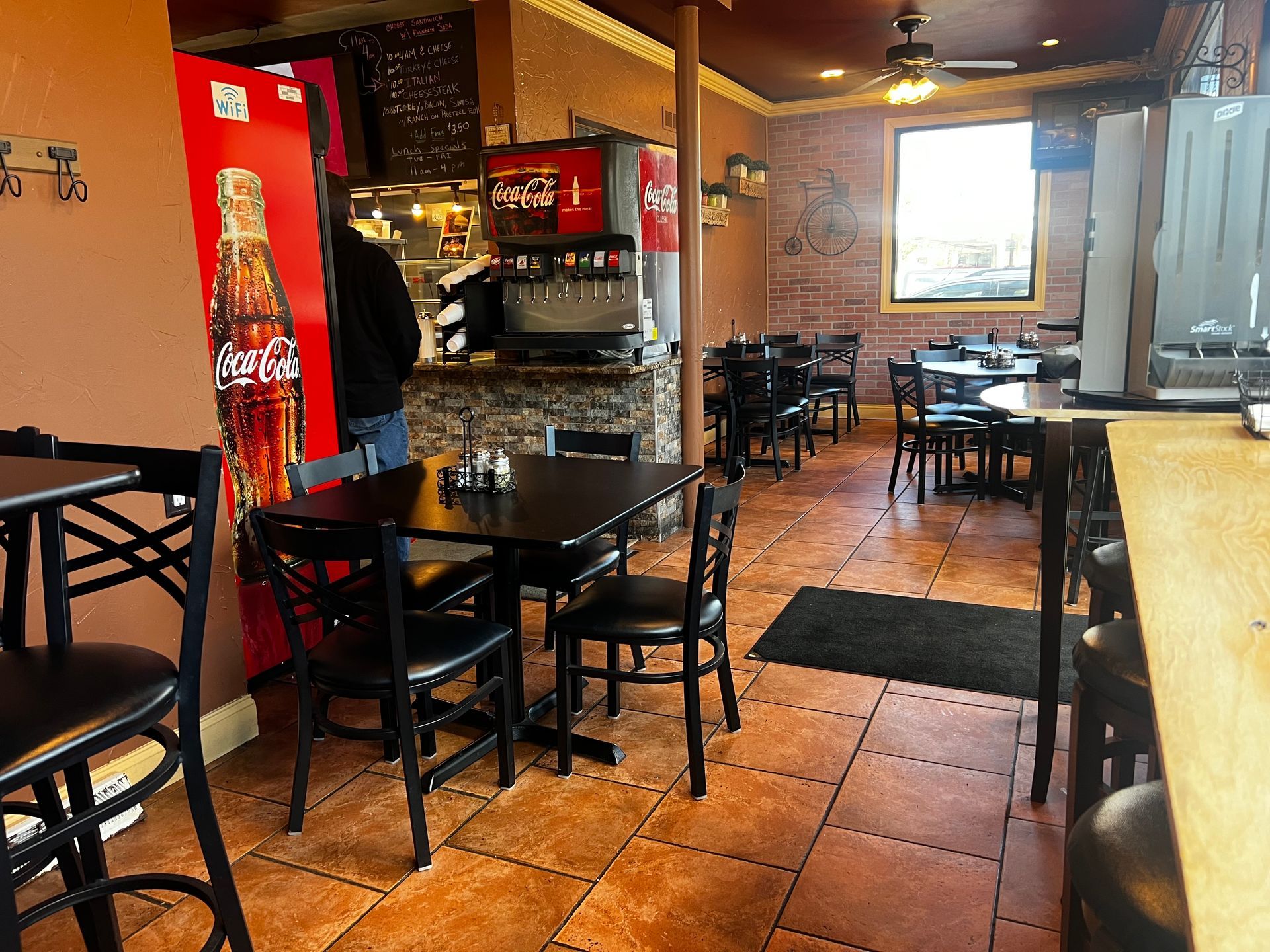 Empty restaurant dining area with black tables and chairs, red wall, and tiled floor.