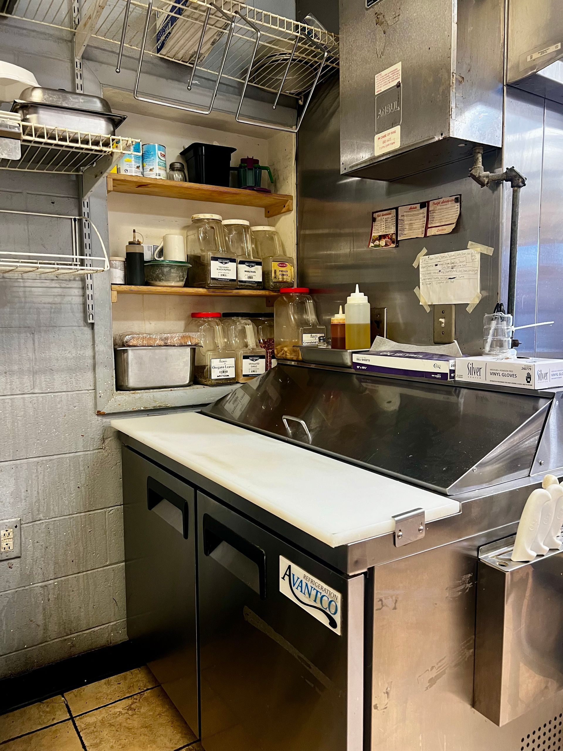 Commercial kitchen prep area with stainless steel counters, shelves, and cleaning supplies under bright lighting