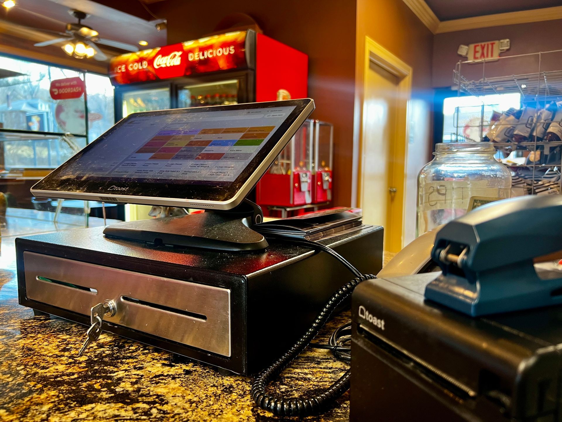 Point-of-sale touchscreen register on a counter in a brightly lit deli or sandwich shop