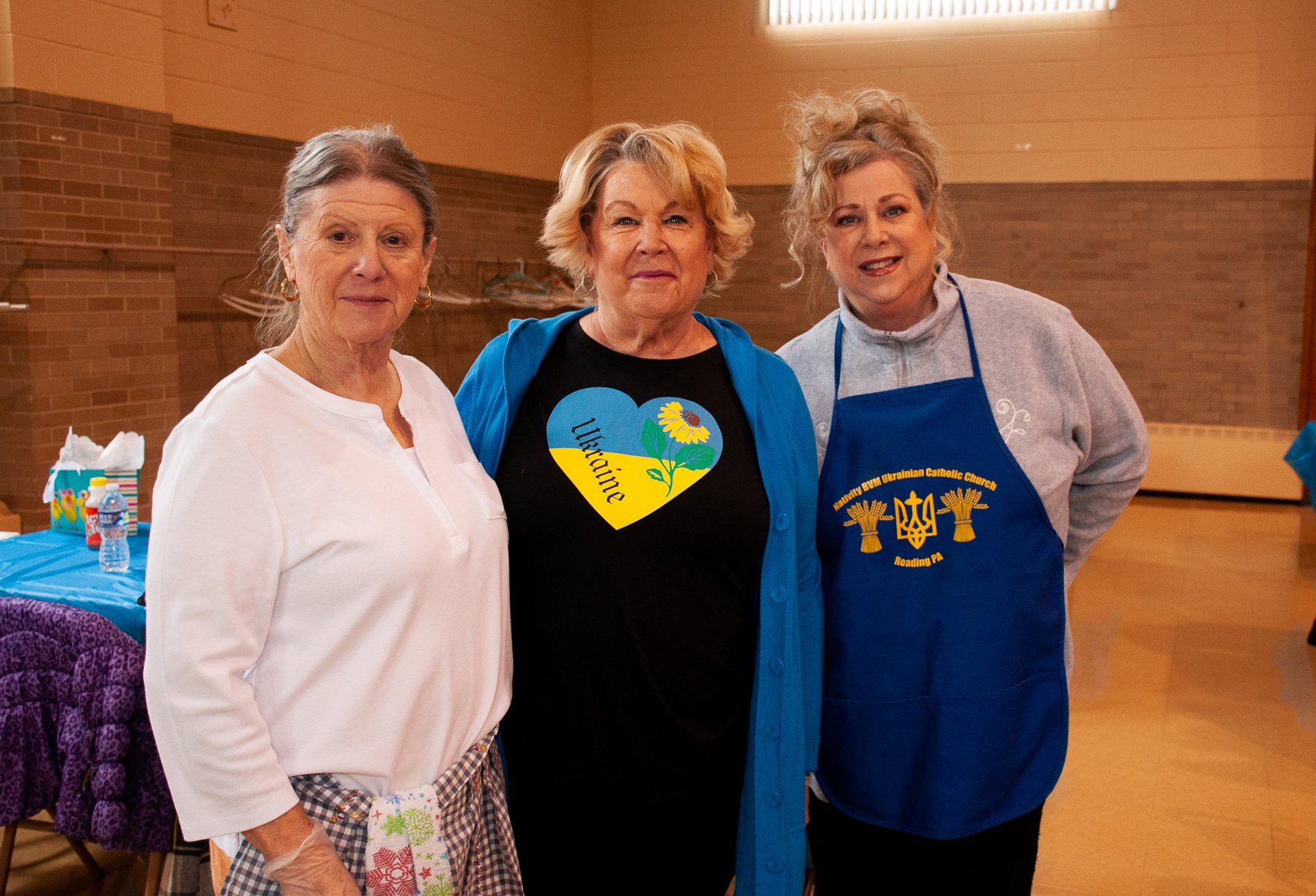 Three people standing indoors, wearing aprons and smiling in a gymnasium.