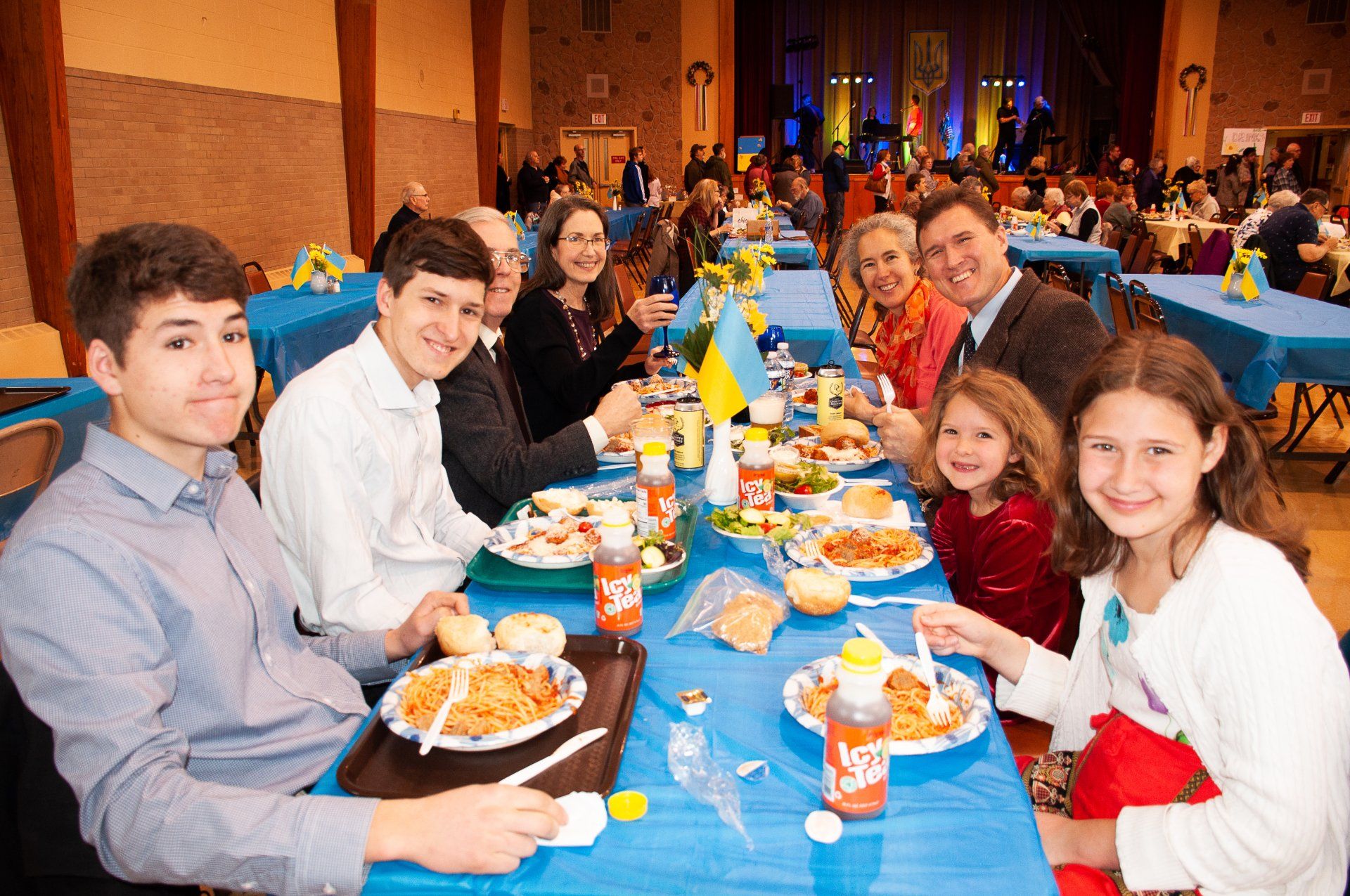 People dining at a banquet table with blue tablecloths, smiling in a decorated hall