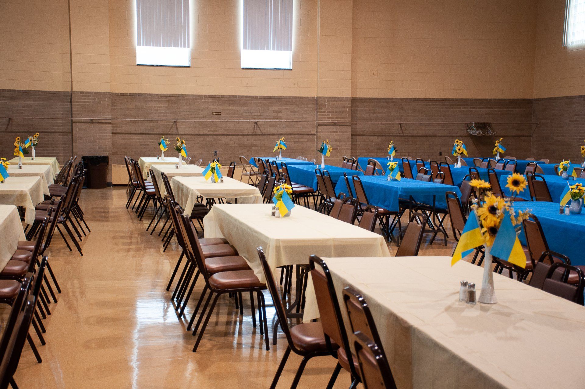 Decorated banquet hall with long tables, chairs, and blue-and-yellow centerpieces set up for an event