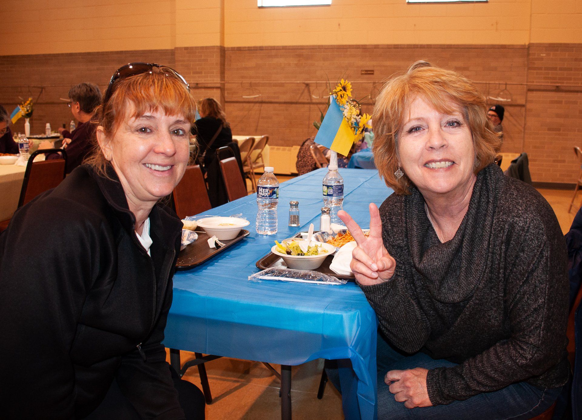 Two women seated at a table in a restaurant, smiling beside a blue tablecloth and a small Swedish flag.