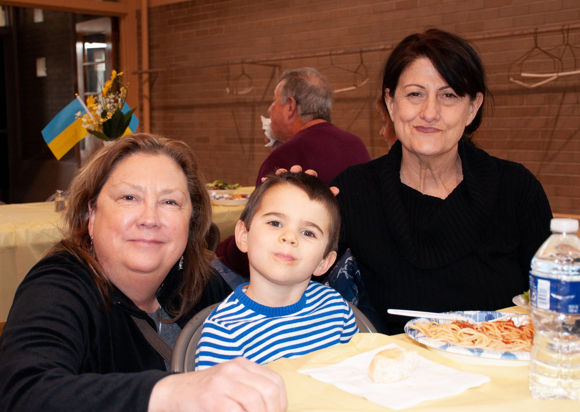 Three people seated at a table indoors, with food and a water bottle in front of them.