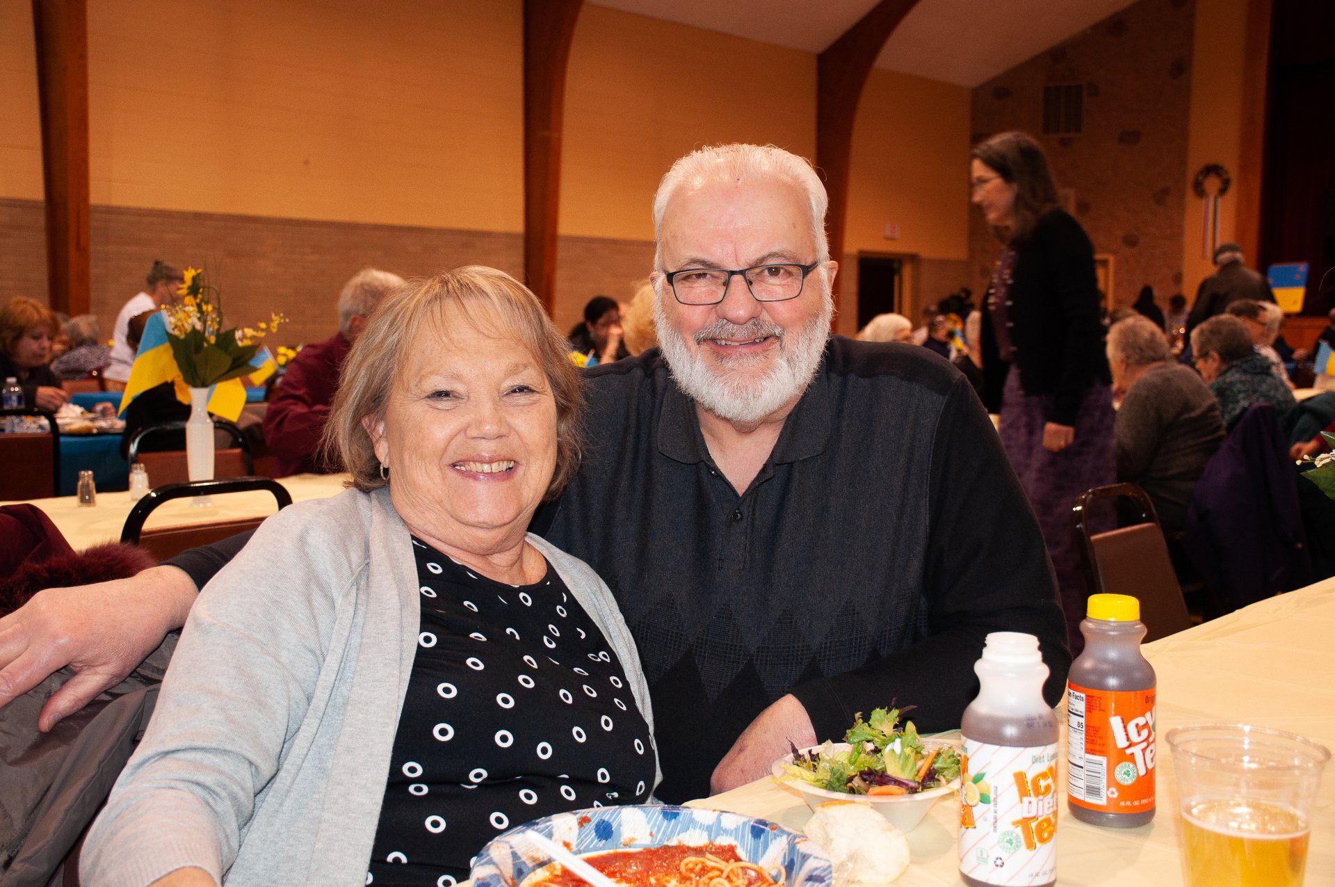 Smiling couple seated at a banquet table with food and drinks in a hall