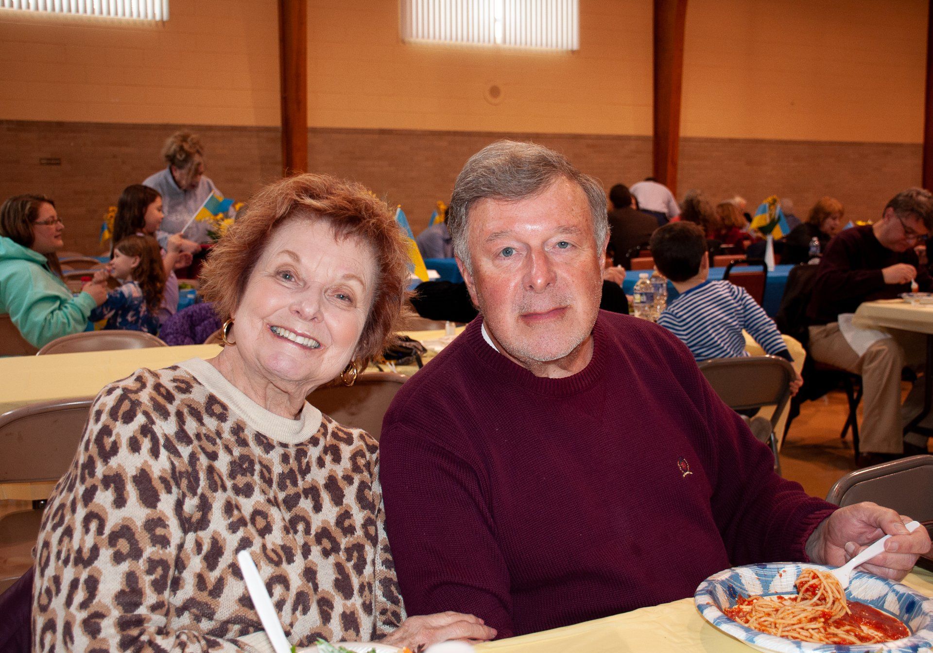 Smiling couple seated at a banquet table, with a plate of food in a warmly lit hall.