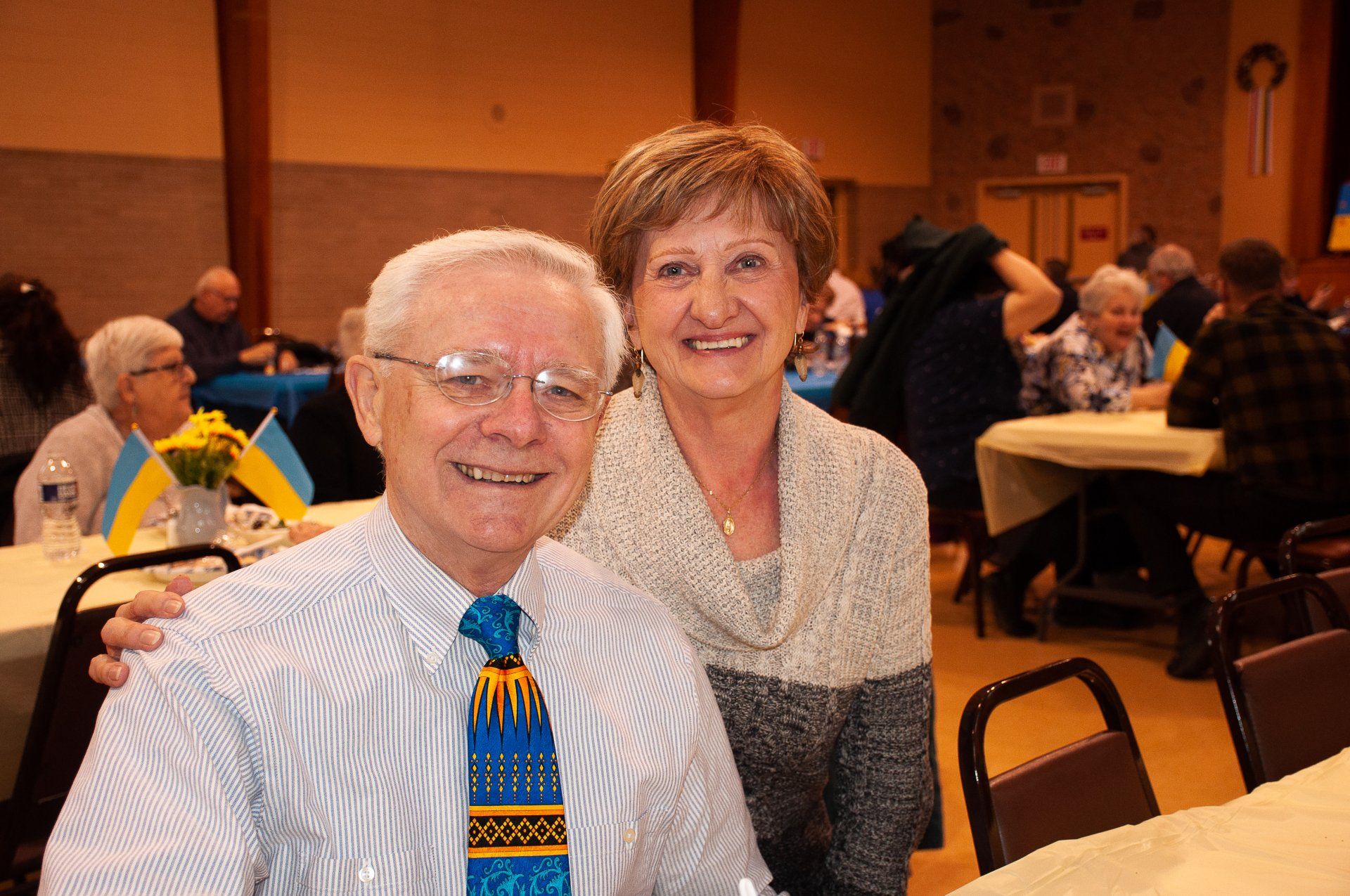 Two smiling people seated at a banquet table in a warmly lit hall