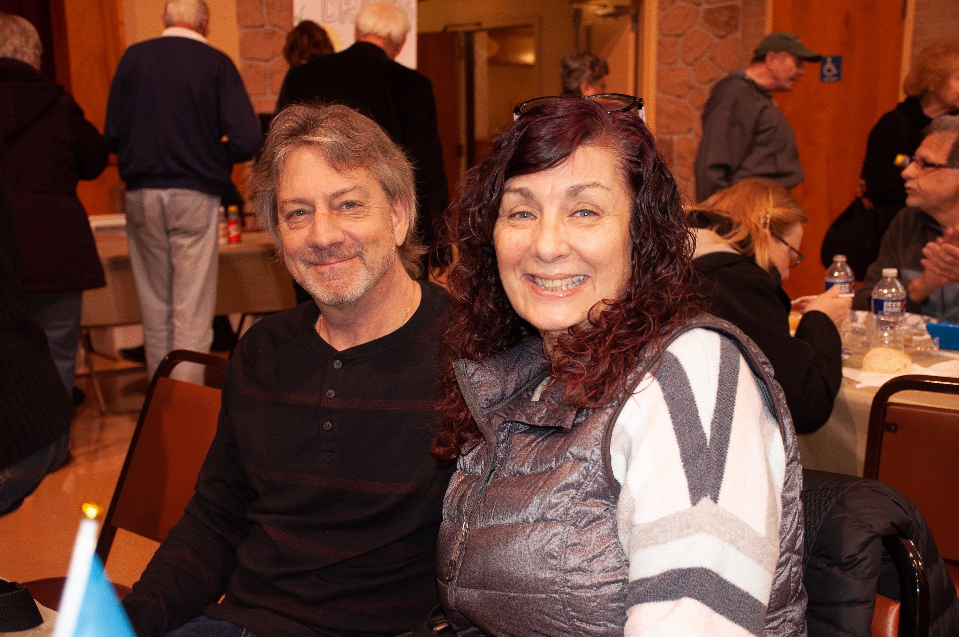Two smiling people seated at a banquet table in a warmly lit indoor hall