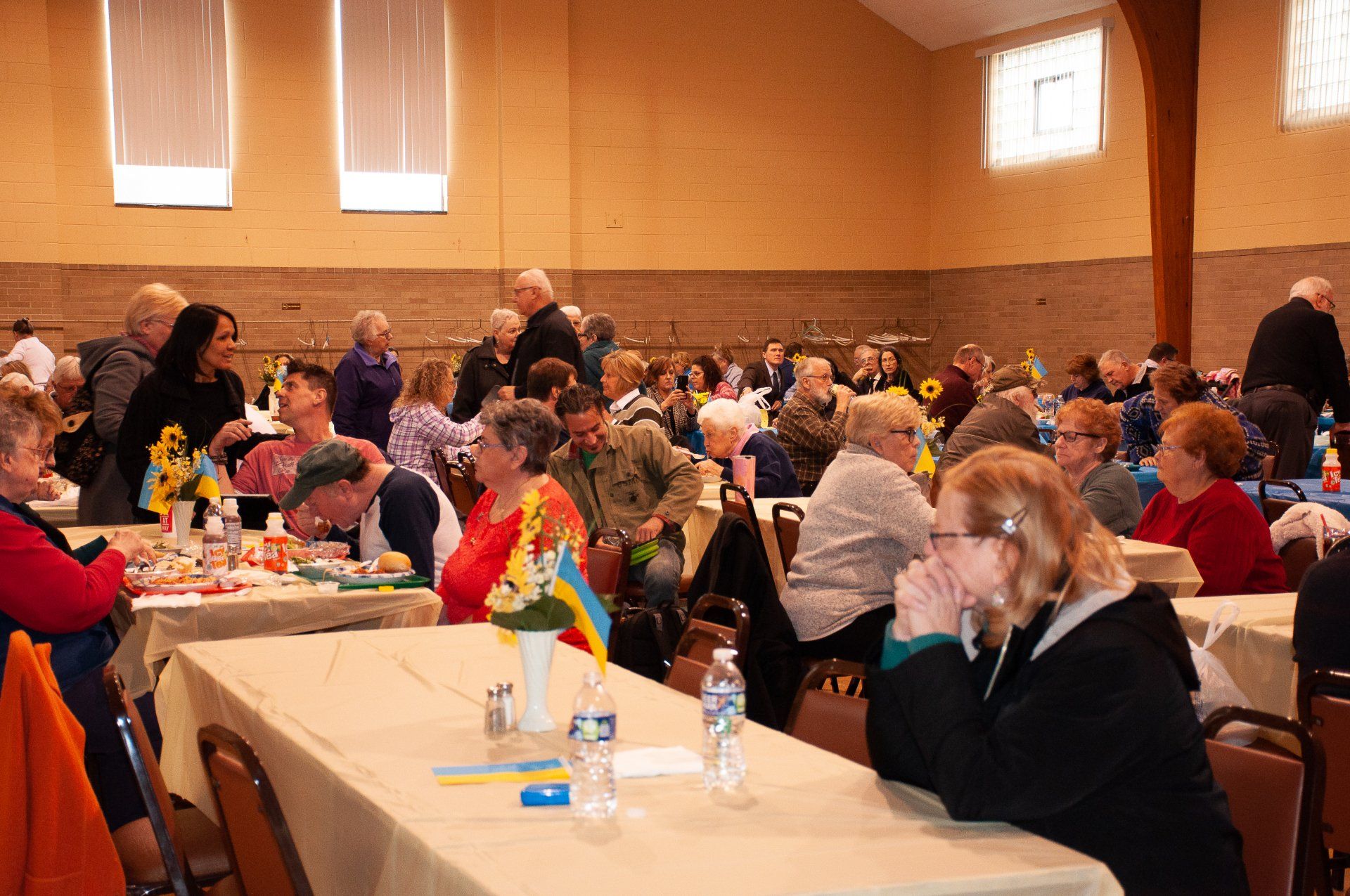People seated at long tables in a brightly lit banquet hall, attending a group event