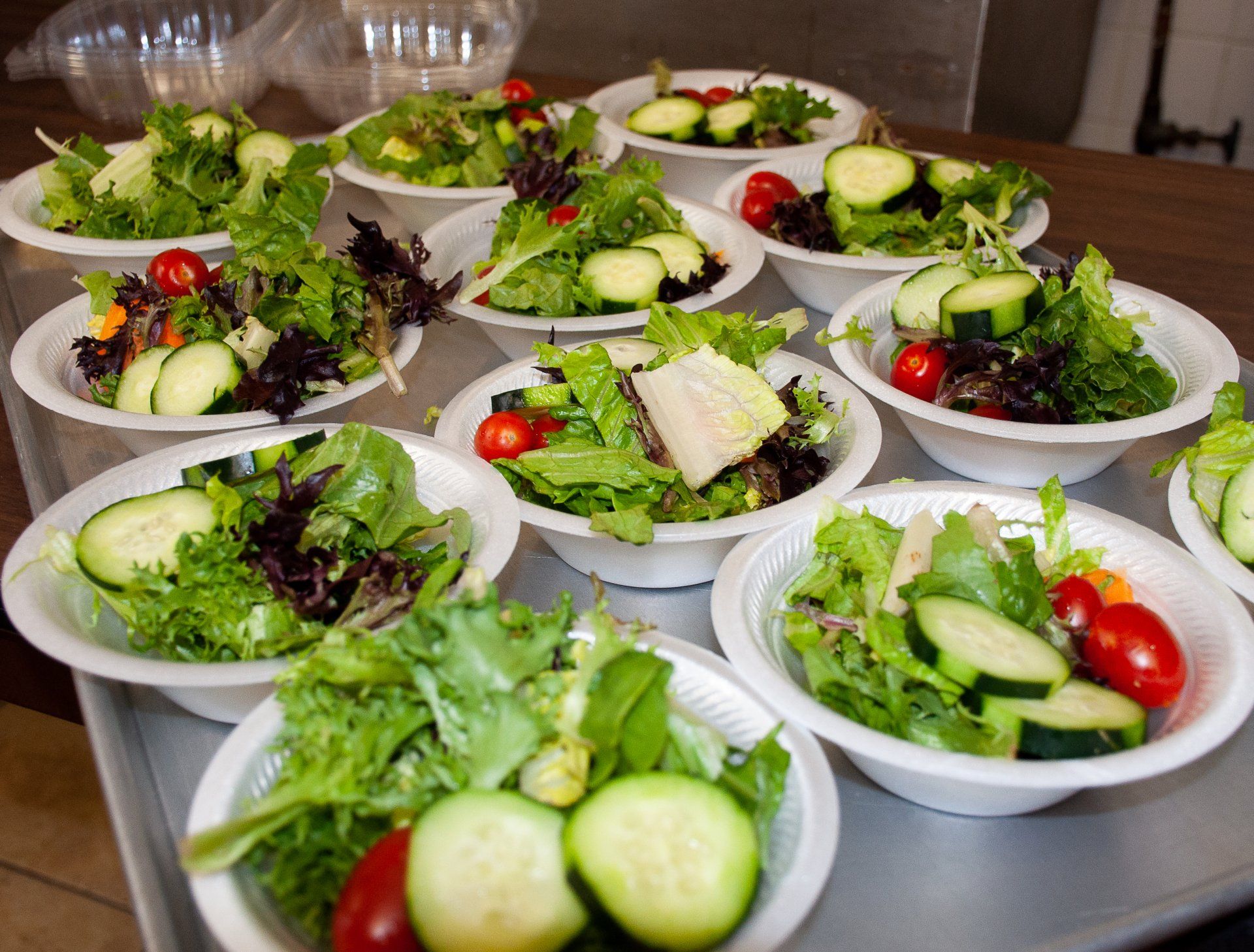 Bowls of mixed green salads with cucumbers, cherry tomatoes, and cheese arranged on a counter