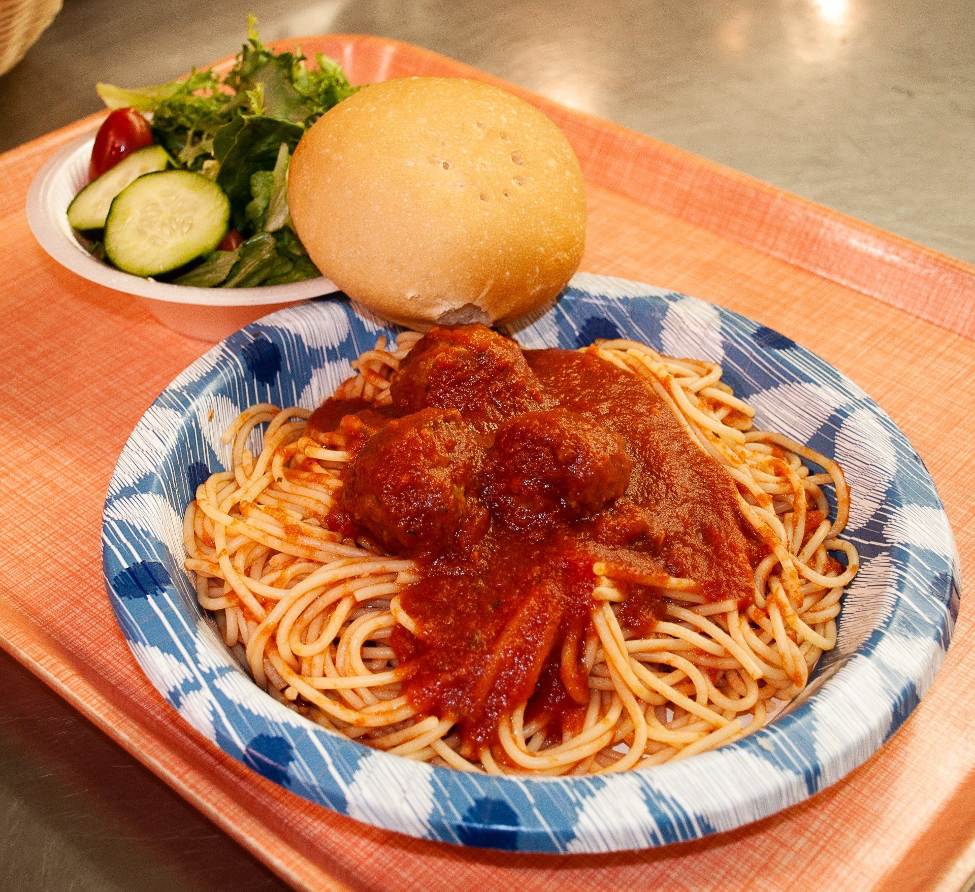 Spaghetti with red sauce and a bread roll on a tray, with a small side salad in the background.