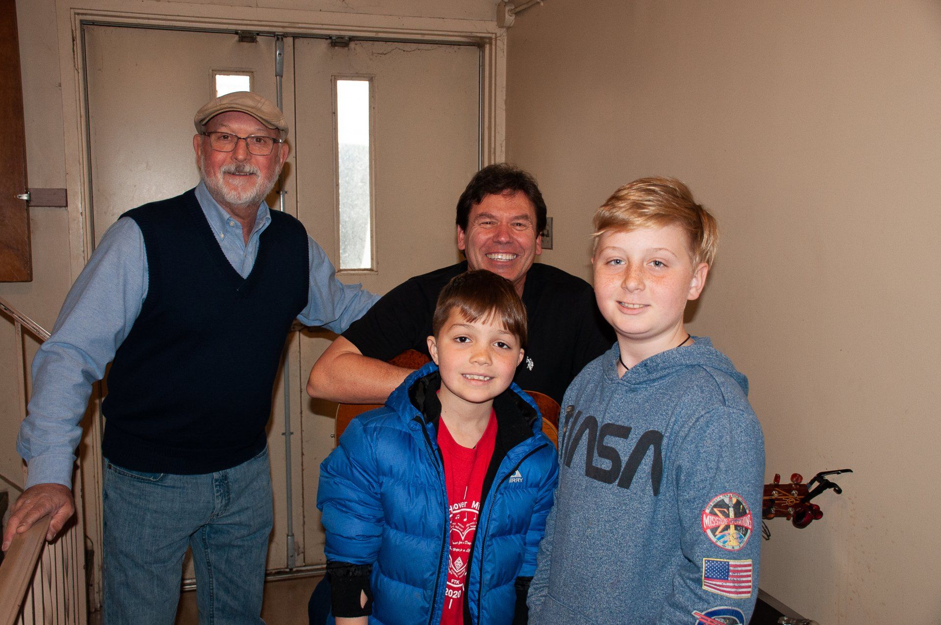Four people smiling indoors, posing near a doorway in casual clothes