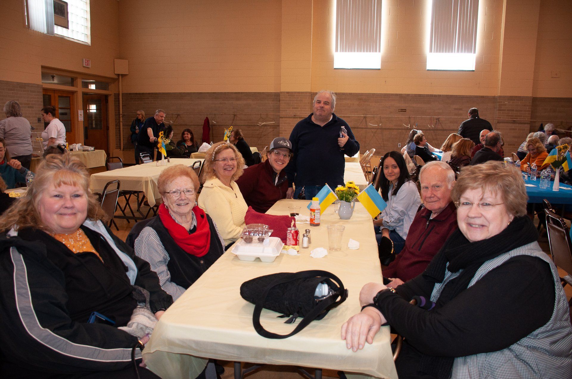 People seated at a banquet table in a community hall, smiling and conversing.