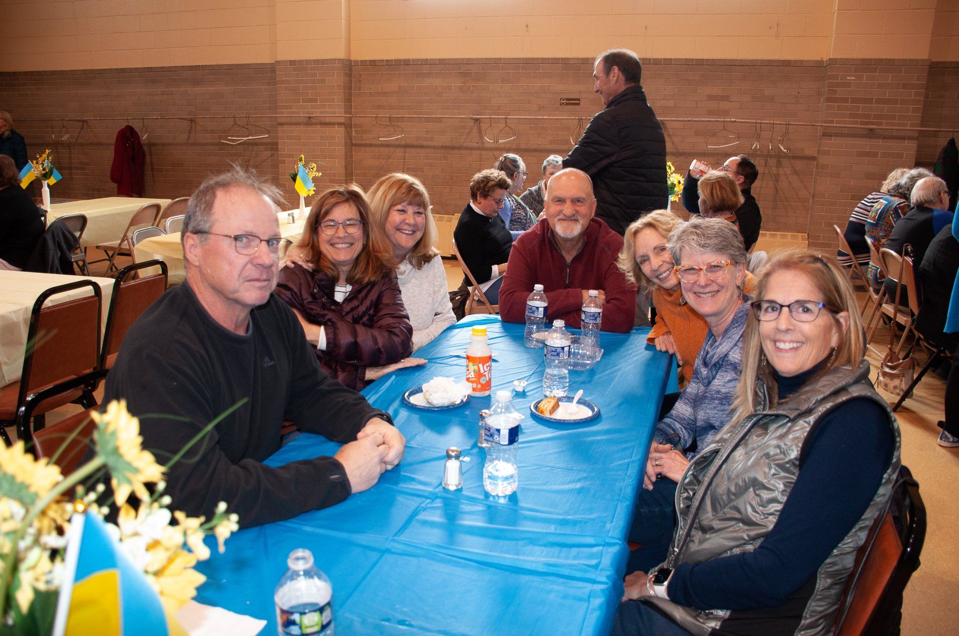 People seated at a blue table in a banquet hall, smiling and chatting with drinks and flowers nearby