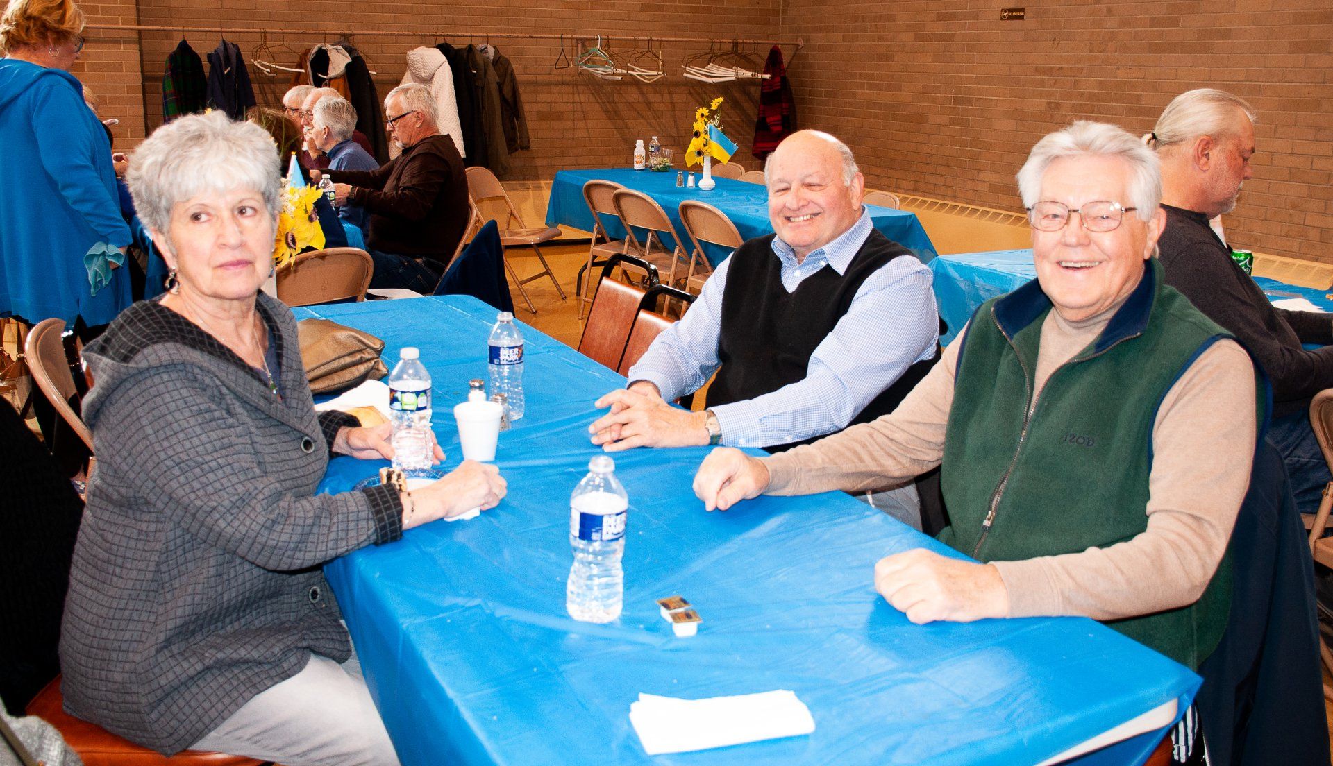 Four people sit at a blue table in a gym-like hall, smiling with water bottles and cups.