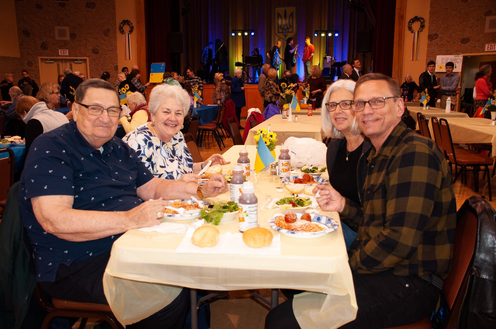 Four people seated at a banquet table with food and drinks in a warmly lit event hall