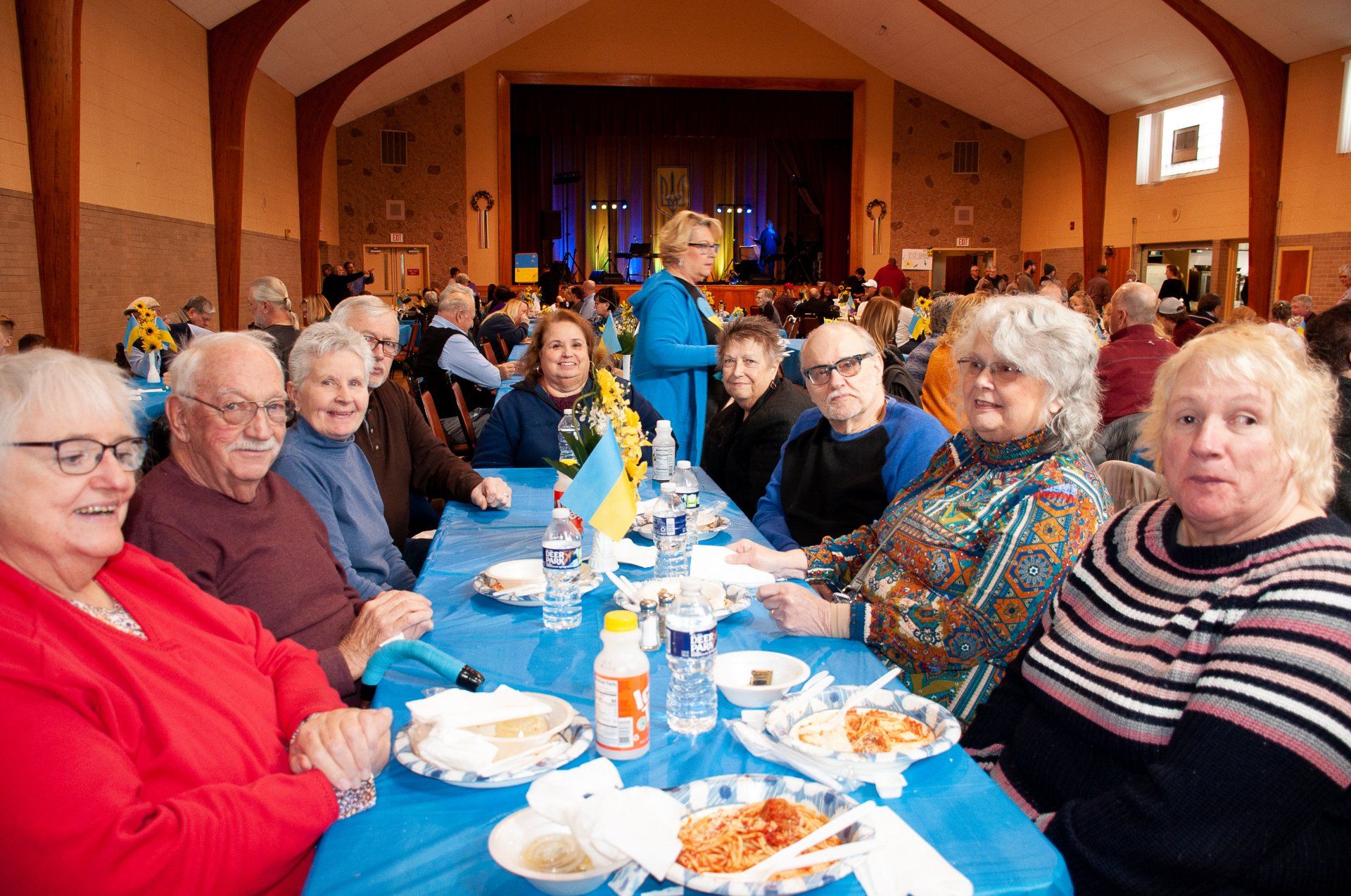 People seated at a long banquet table in a hall, sharing food and drinks.