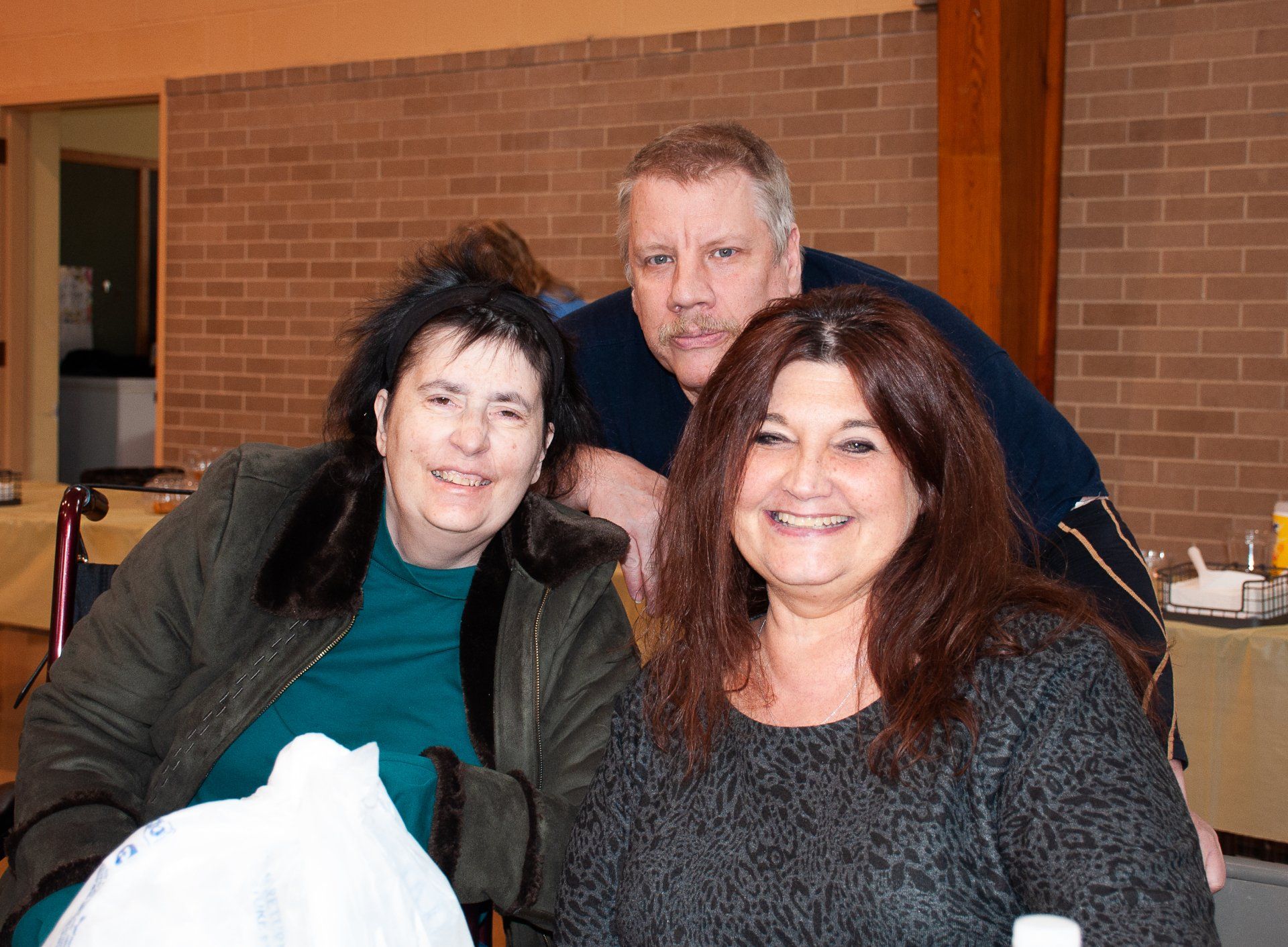Three people smiling indoors, seated close together in a warm-lit room.