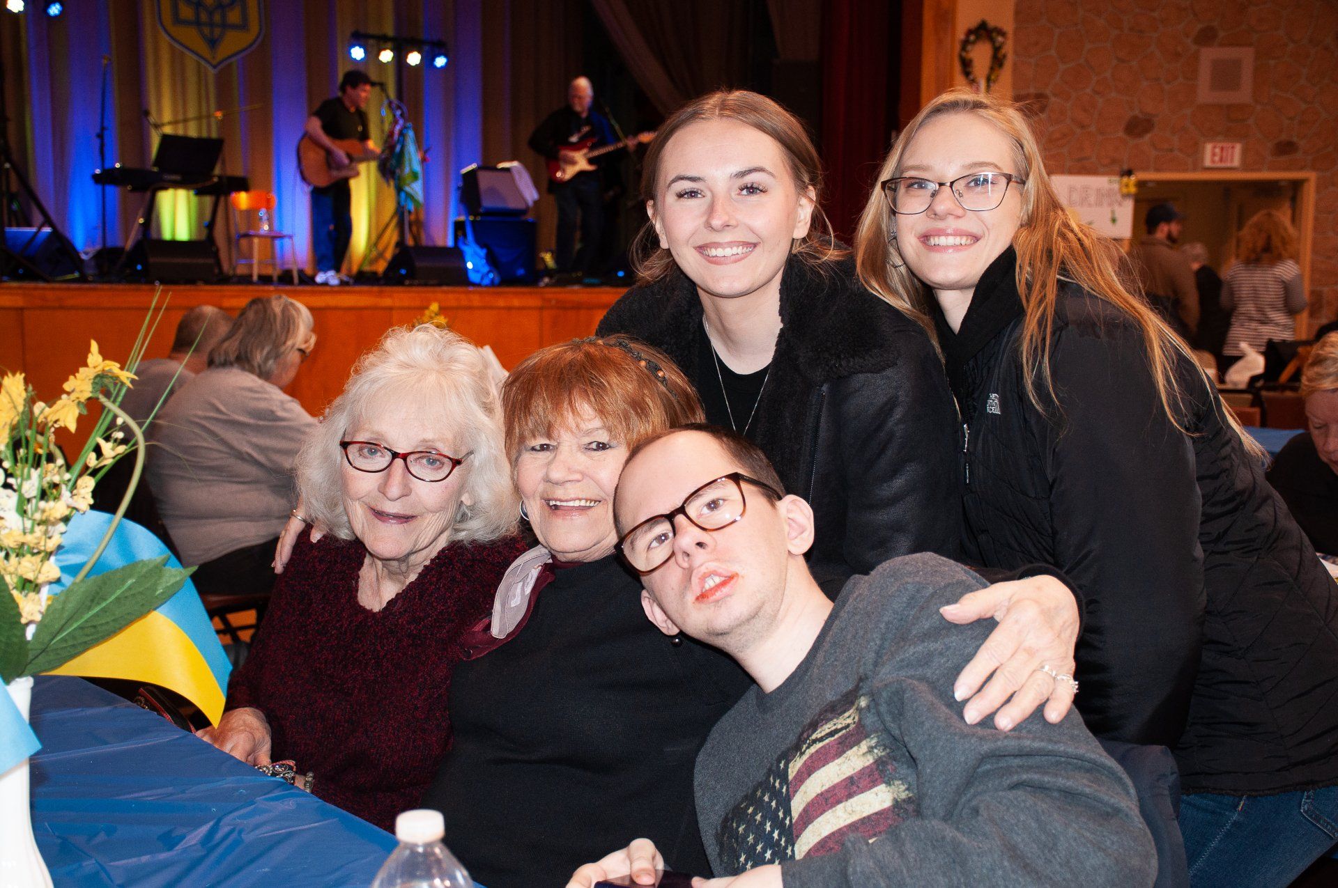 Group posing at a lively indoor event, with smiles and a stage performance in the background.