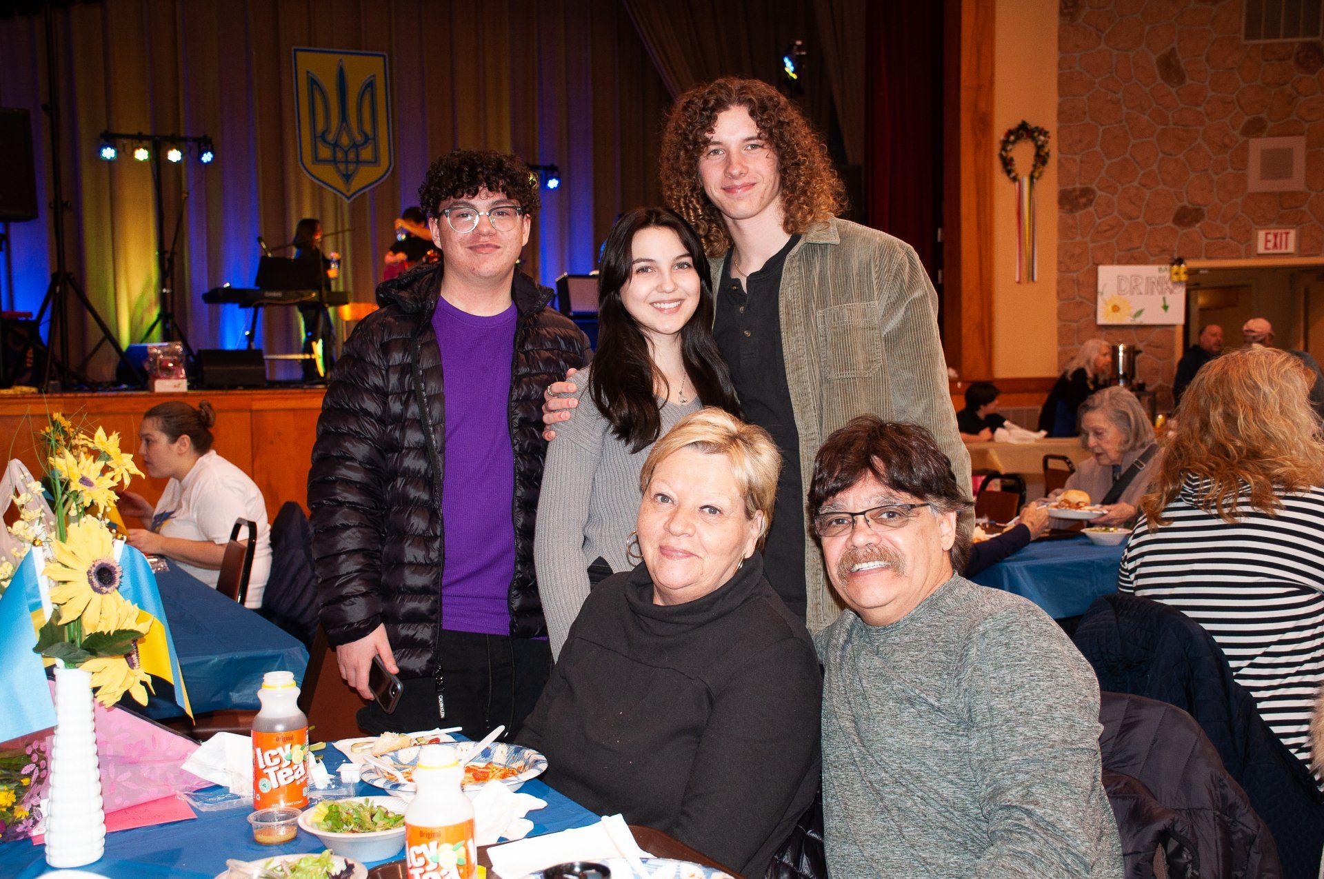 Five people posing at a banquet table in a warmly lit event hall, with food and drinks in front of them