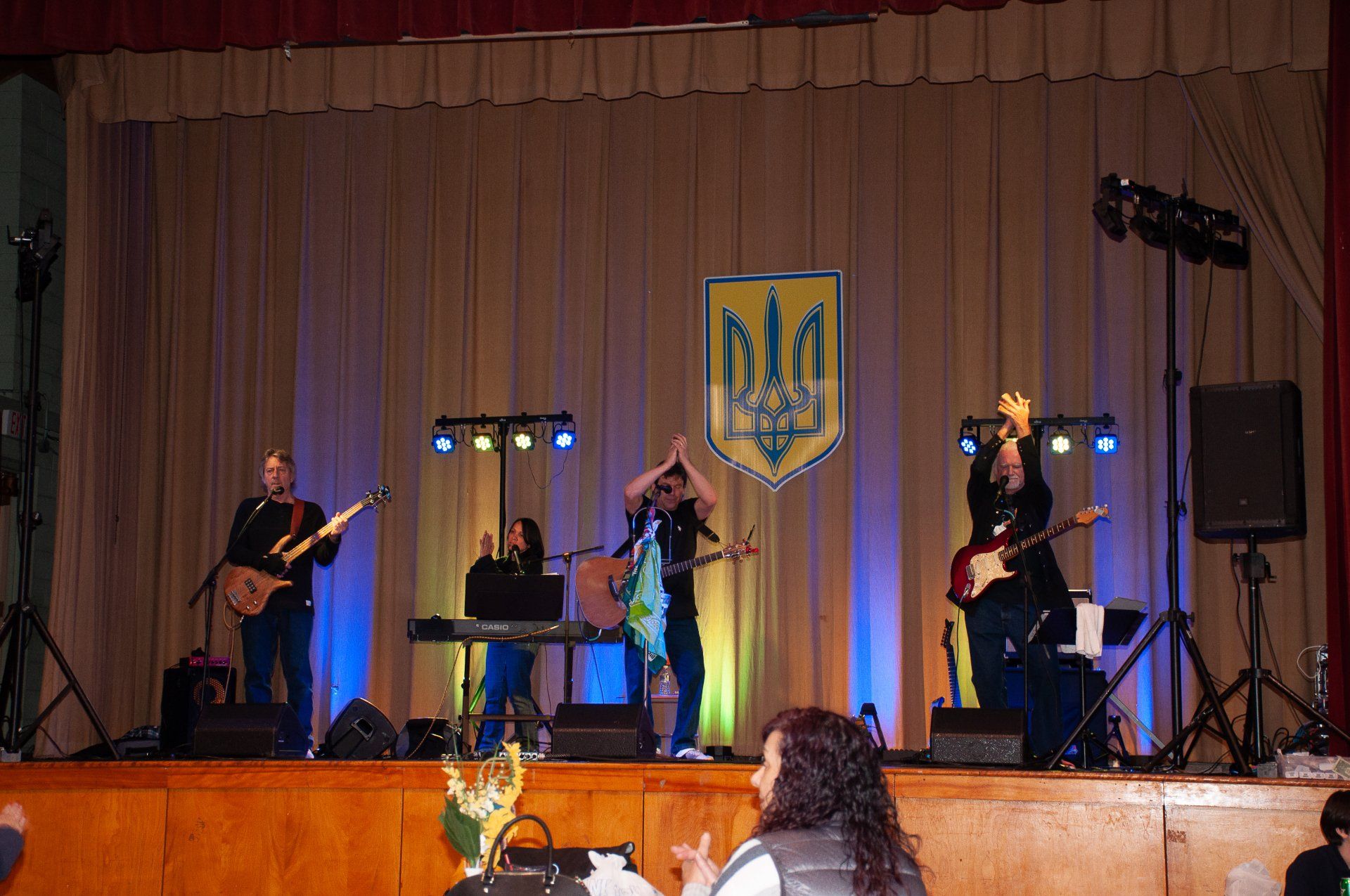 Band performing on a stage with blue and purple lights and a Ukraine emblem backdrop