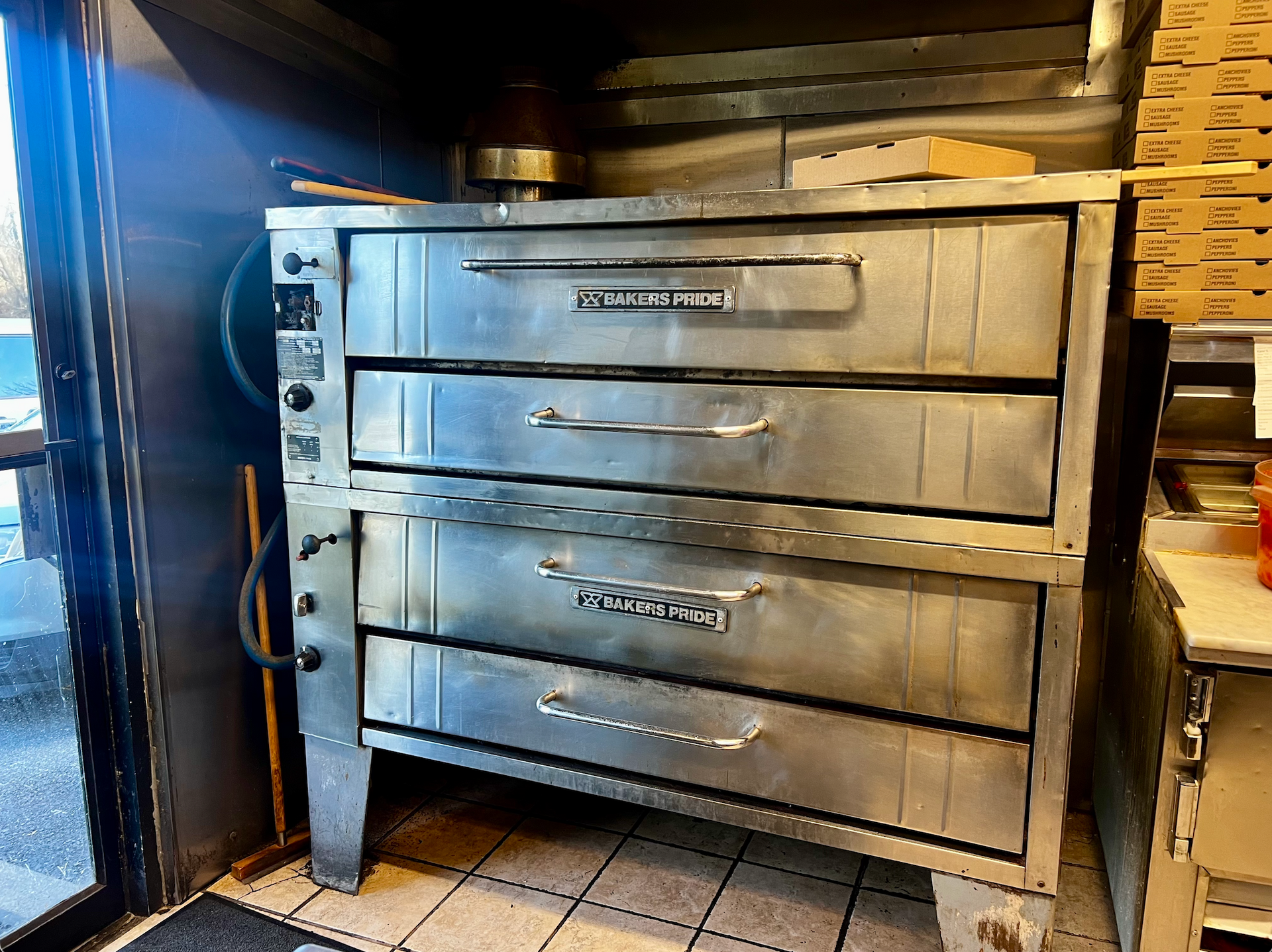 Stainless steel commercial oven with four stacked drawers in a tiled kitchen area.