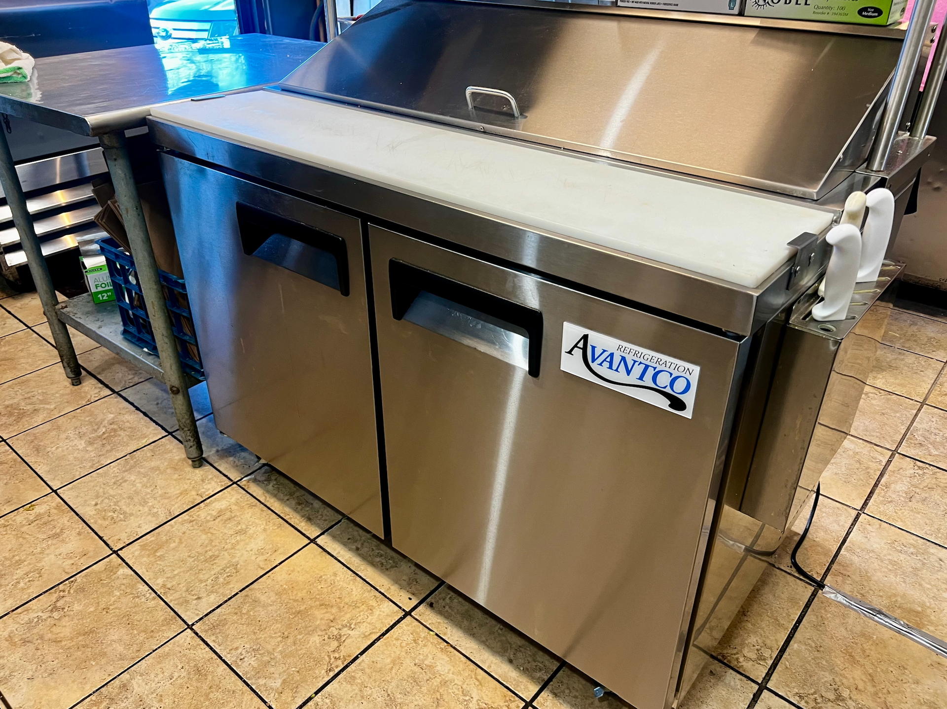 Stainless steel commercial refrigerator or freezer with doors and drawers in a tiled kitchen or restaurant.
