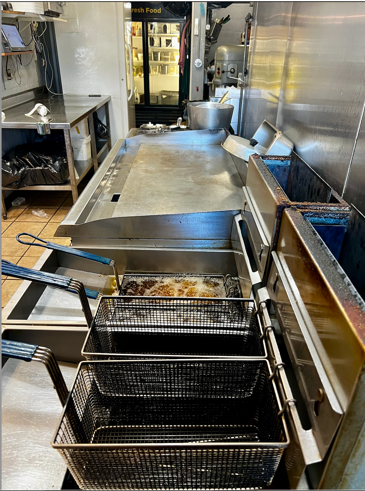 Commercial kitchen with fryer baskets, stainless prep table, and sink along the right wall.