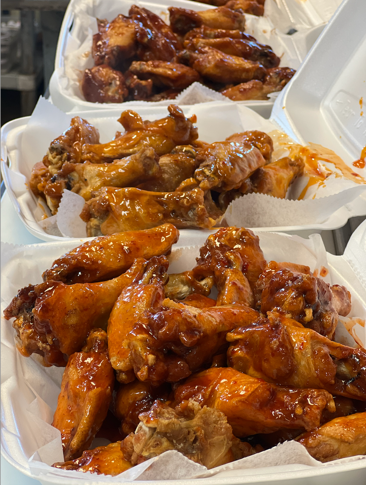 Takeout containers filled with glazed chicken wings and dipping sauce