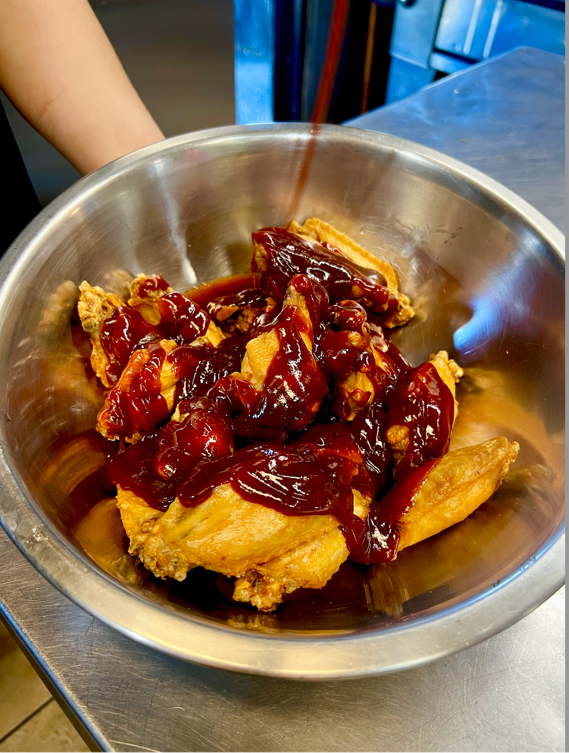 Metal bowl of fried food topped with glossy red sauce on a stainless steel counter