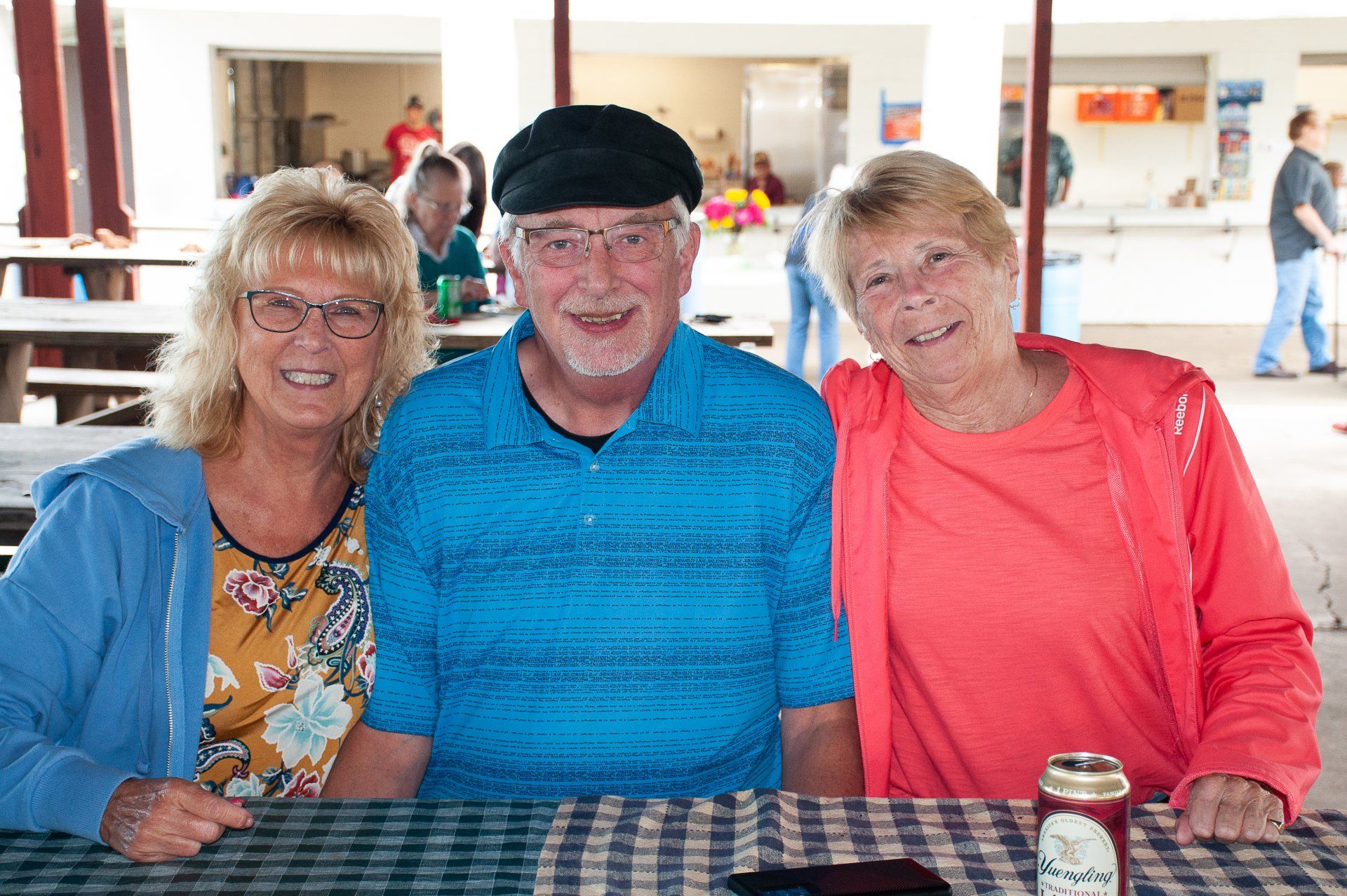 Three smiling people seated at a table in a bright cafeteria, wearing blue, teal, and coral tops.
