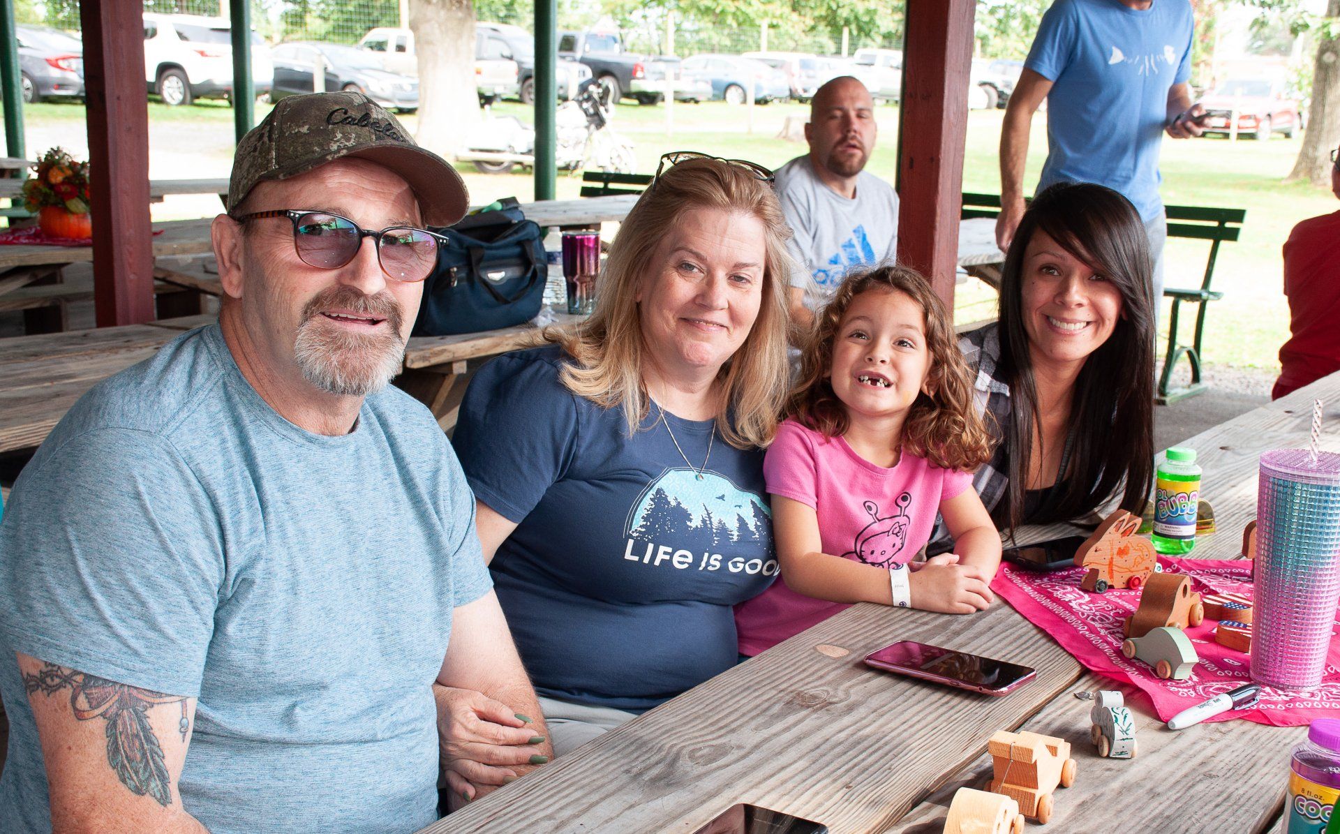 Family seated at a picnic table under a pavilion, smiling with drinks and snacks.