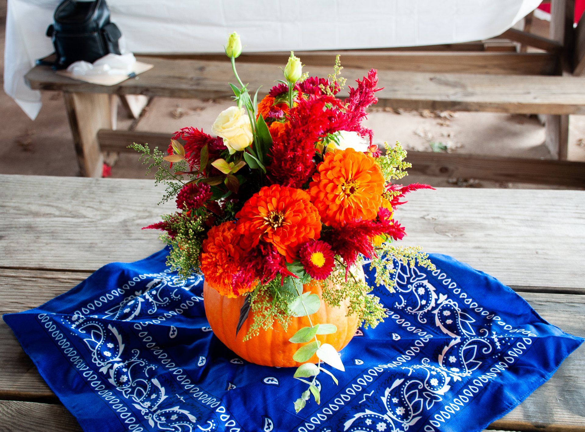 Orange pumpkin vase with colorful flowers on a blue cloth-covered wooden table