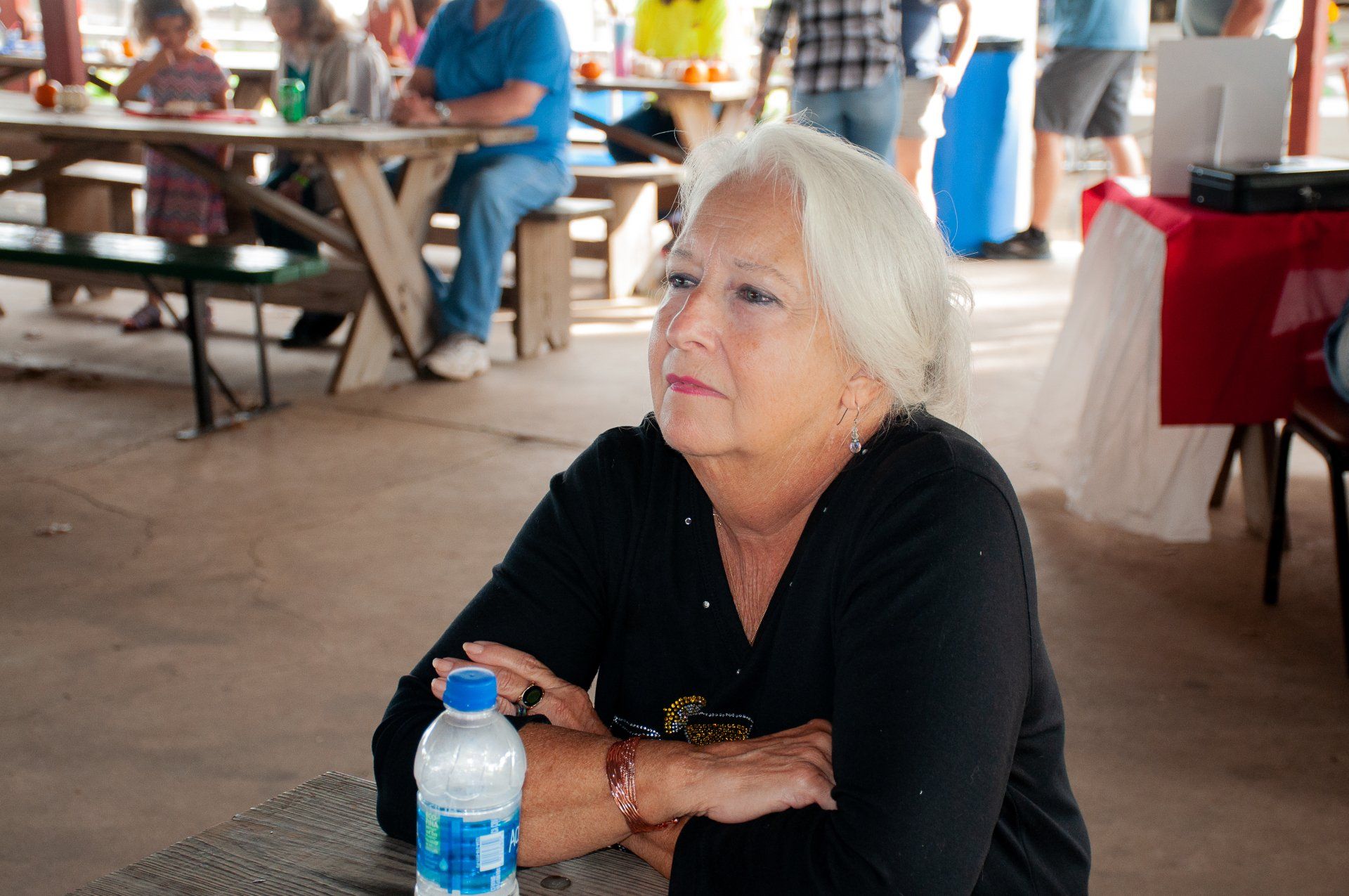 Woman seated at a picnic table with a water bottle in a pavilion, looking off to the side