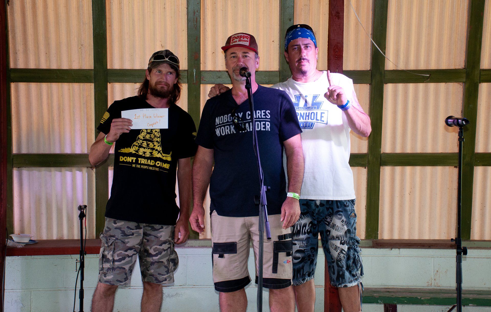 Three men standing on a stage, one holding a certificate, with microphones in front of them.