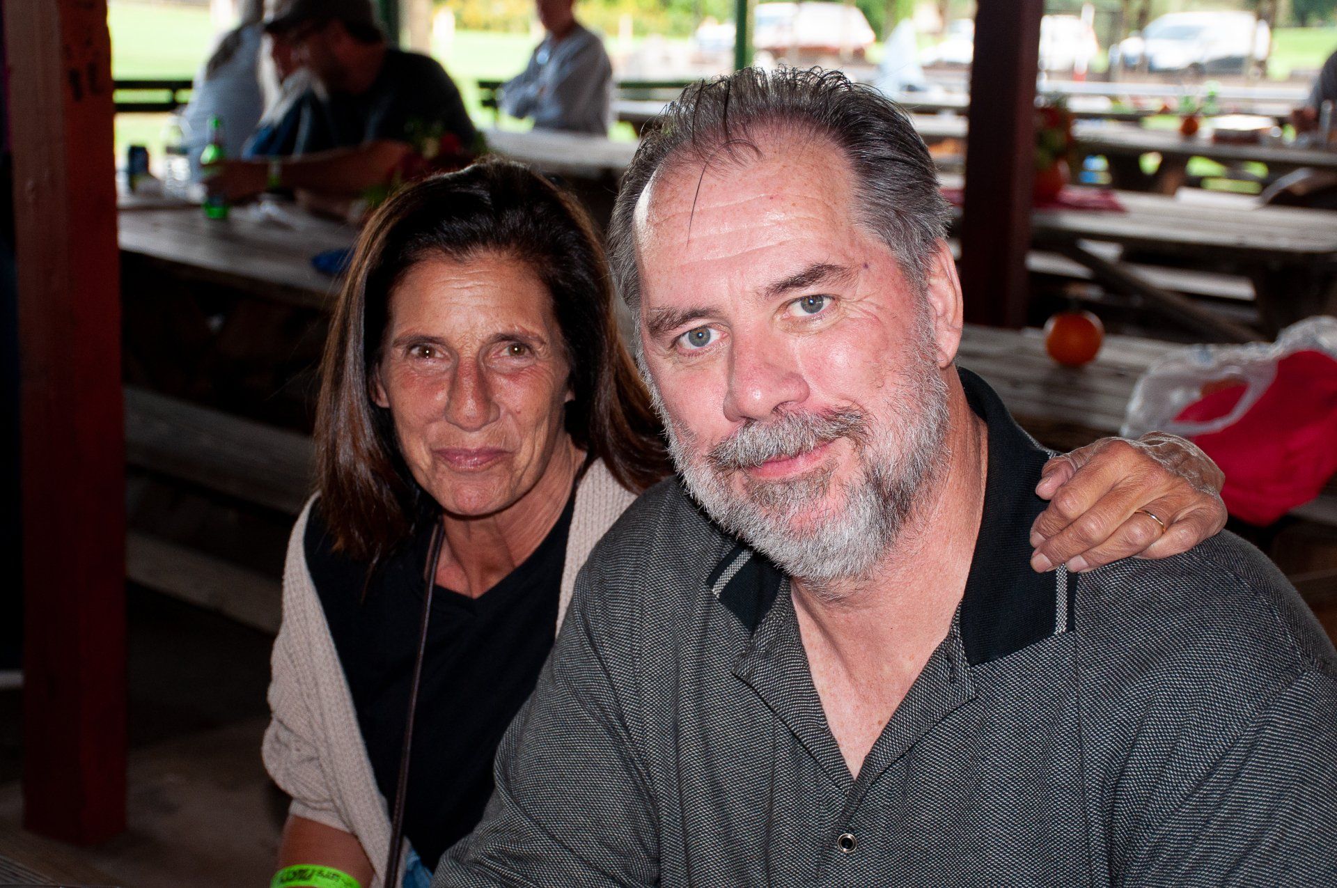 Two people seated at a wooden table, posing together indoors with a casual smile