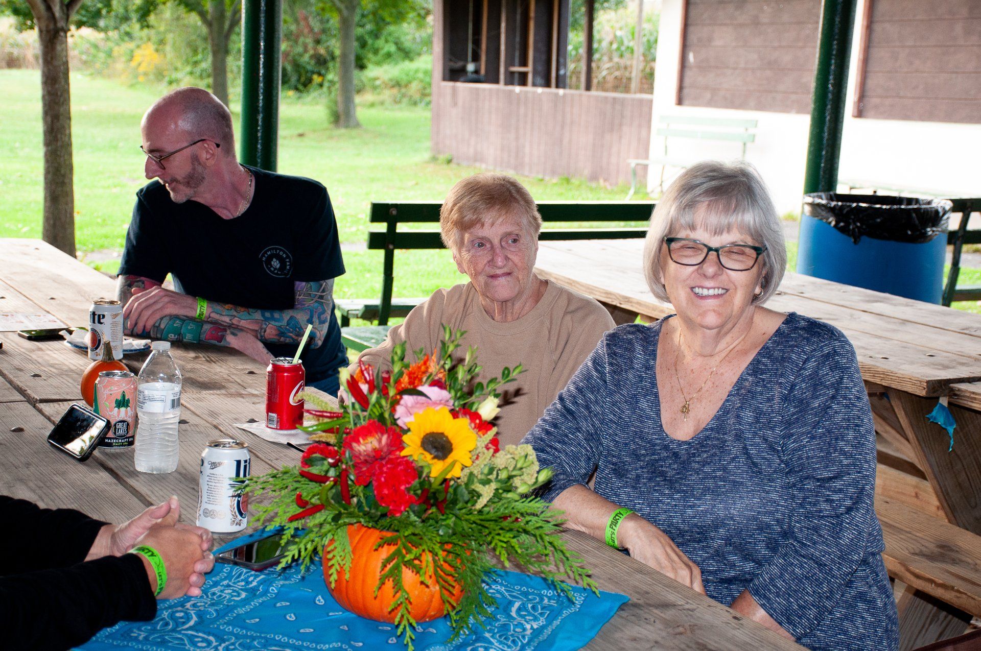 Three people sitting at a picnic table with a bright flower centerpiece in a park pavilion