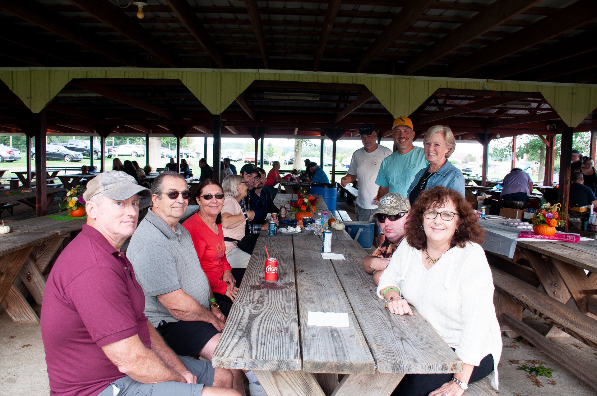 Group sitting at a picnic table in a covered pavilion, chatting and smiling over drinks.
