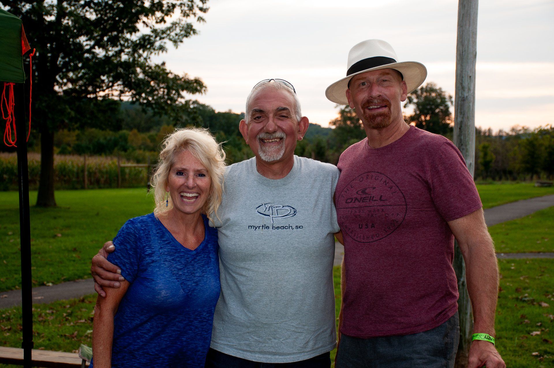 Three people smiling outdoors on a golf course at sunset