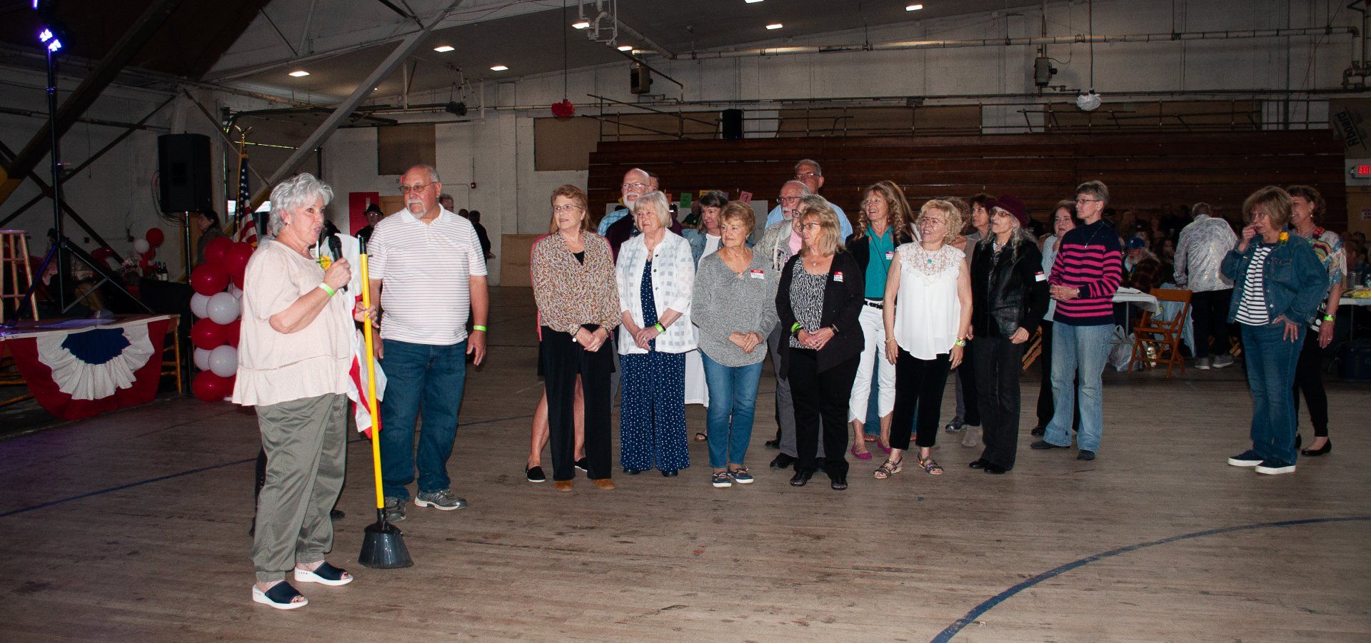 People lined up in a hall, with one person speaking at a microphone near red, white, and blue bunting.